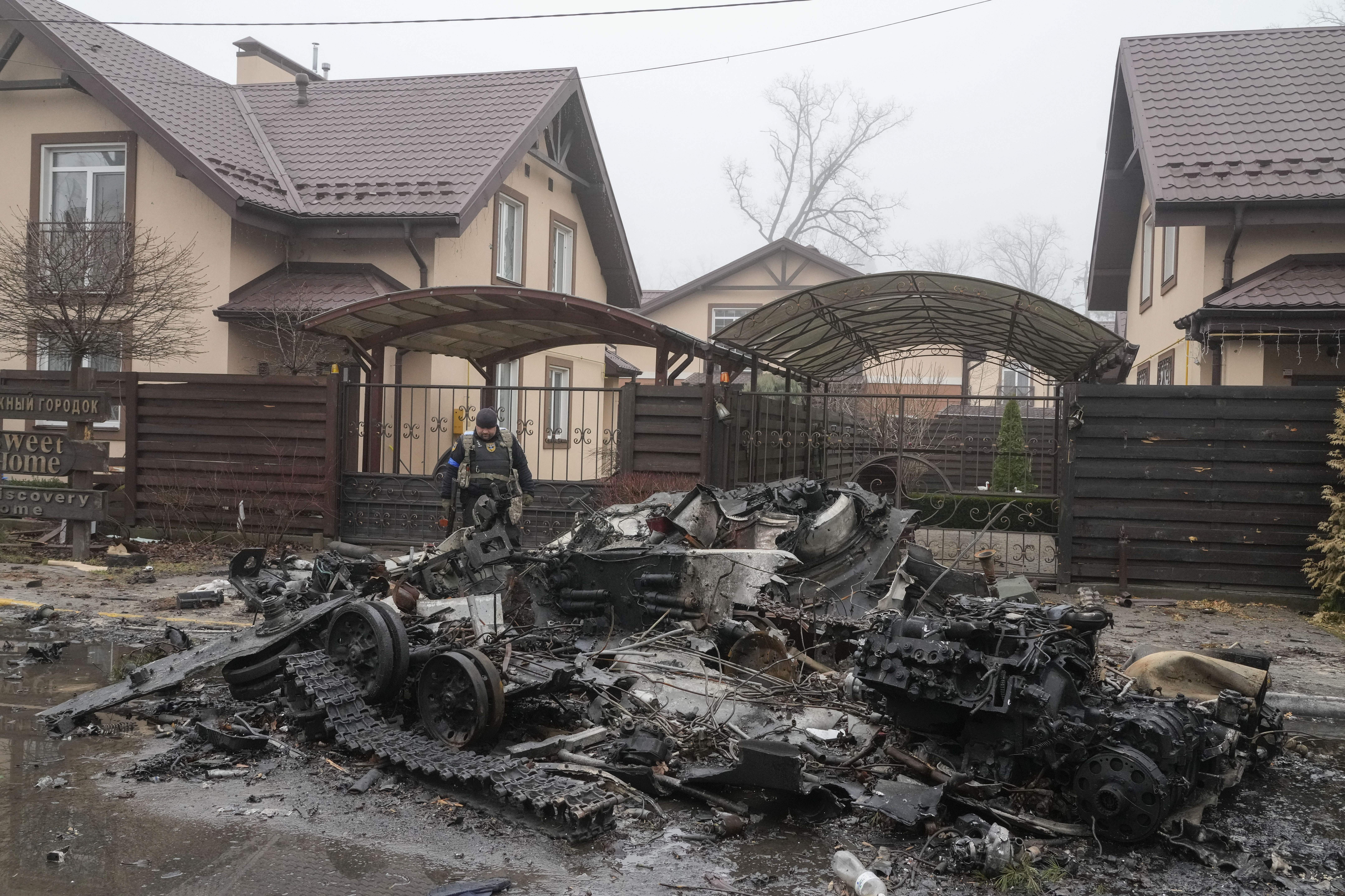 A Ukrainian soldier checks a destroyed Russian tank in front of pink-coloured houses, in Irpin, close to Kyiv, 