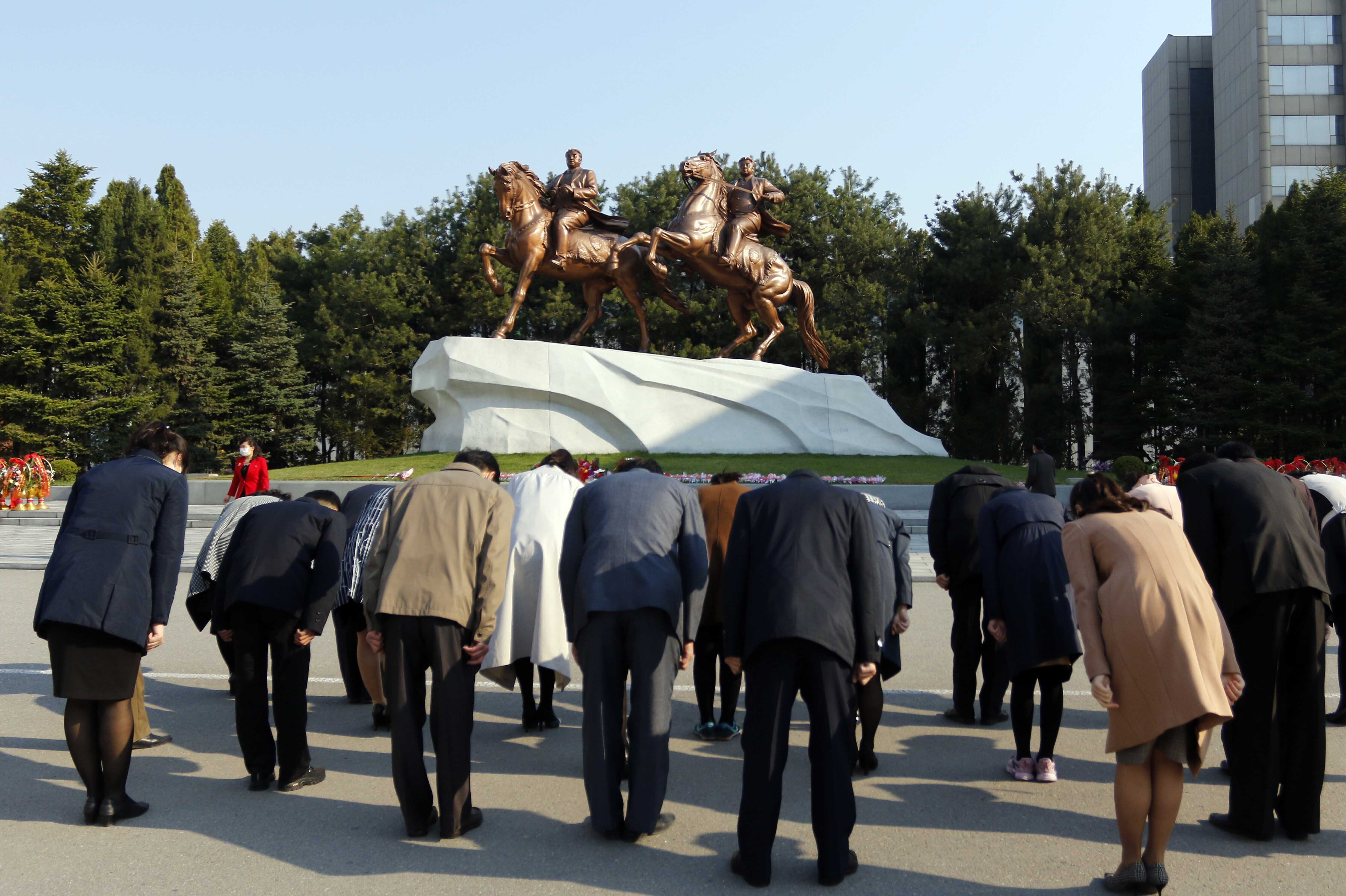 A small group of North Koreans bow towards bronze-coloured statues of Kim Il Sung and Kim Jong Il riding horses