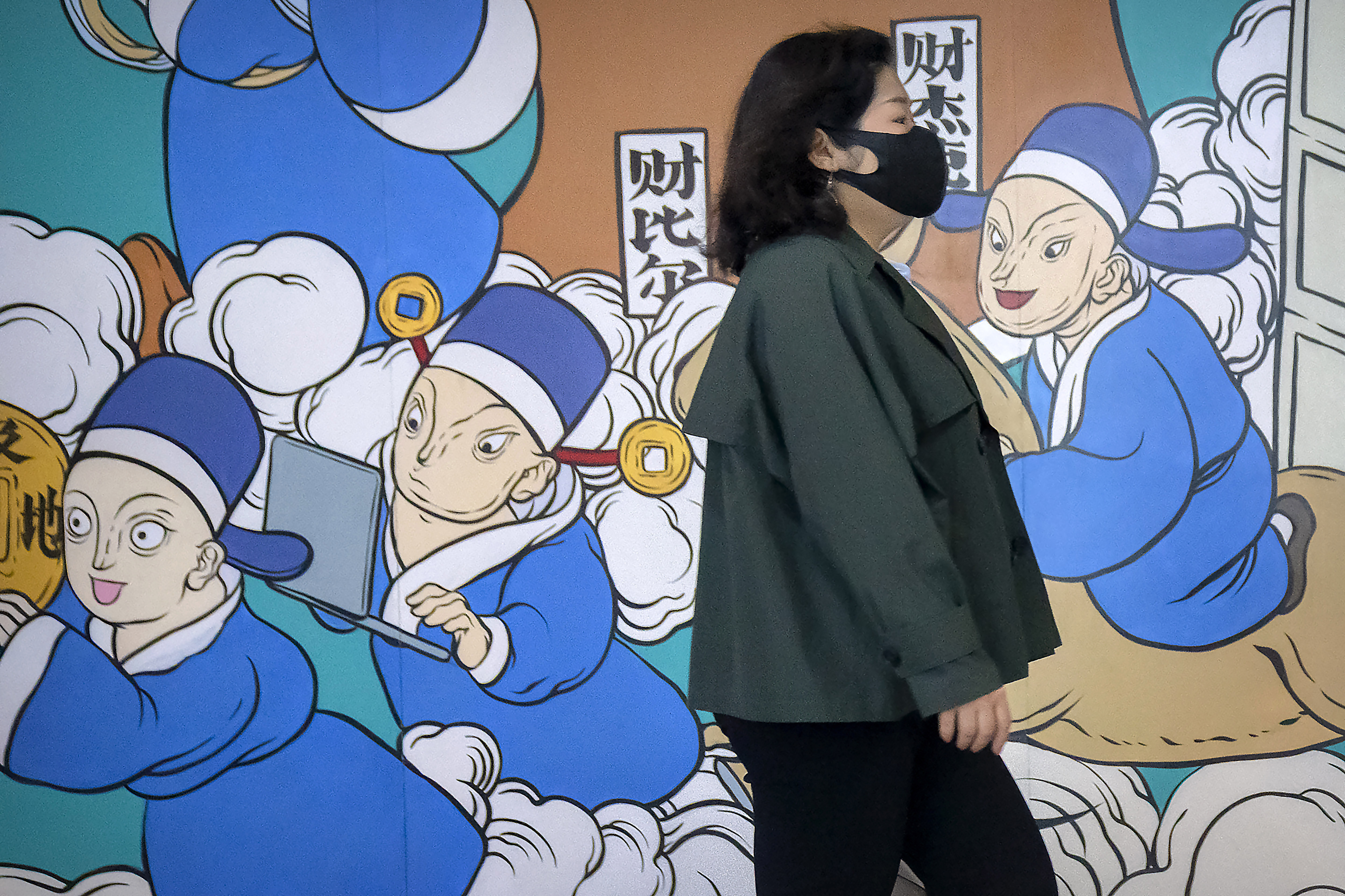 A woman wearing a face mask walks past a mural of healthcare workers in blue medical gowns in Beijing.