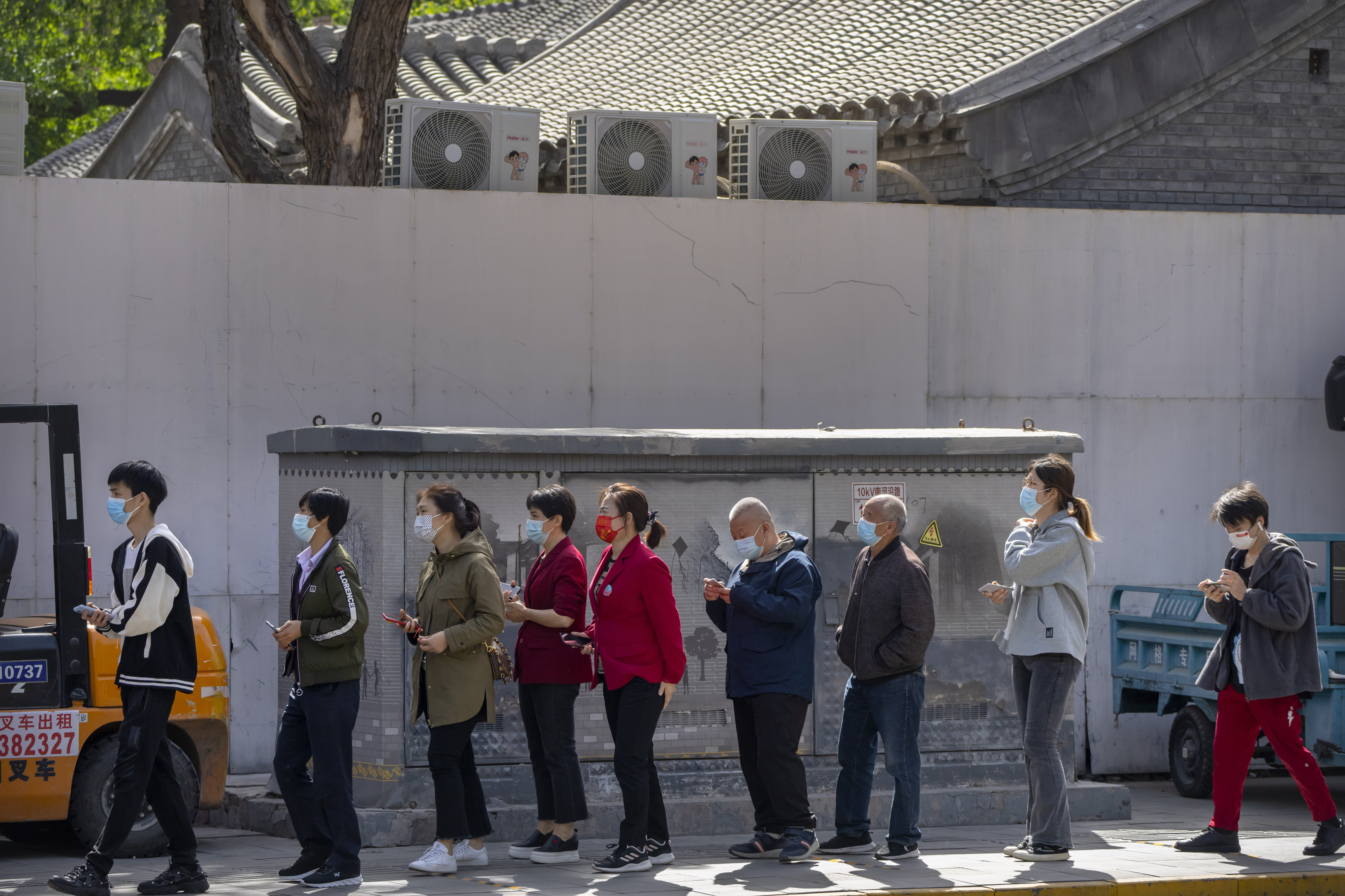 People wearing face masks stand in line for coronavirus tests in a neighborhood in the Dongcheng district