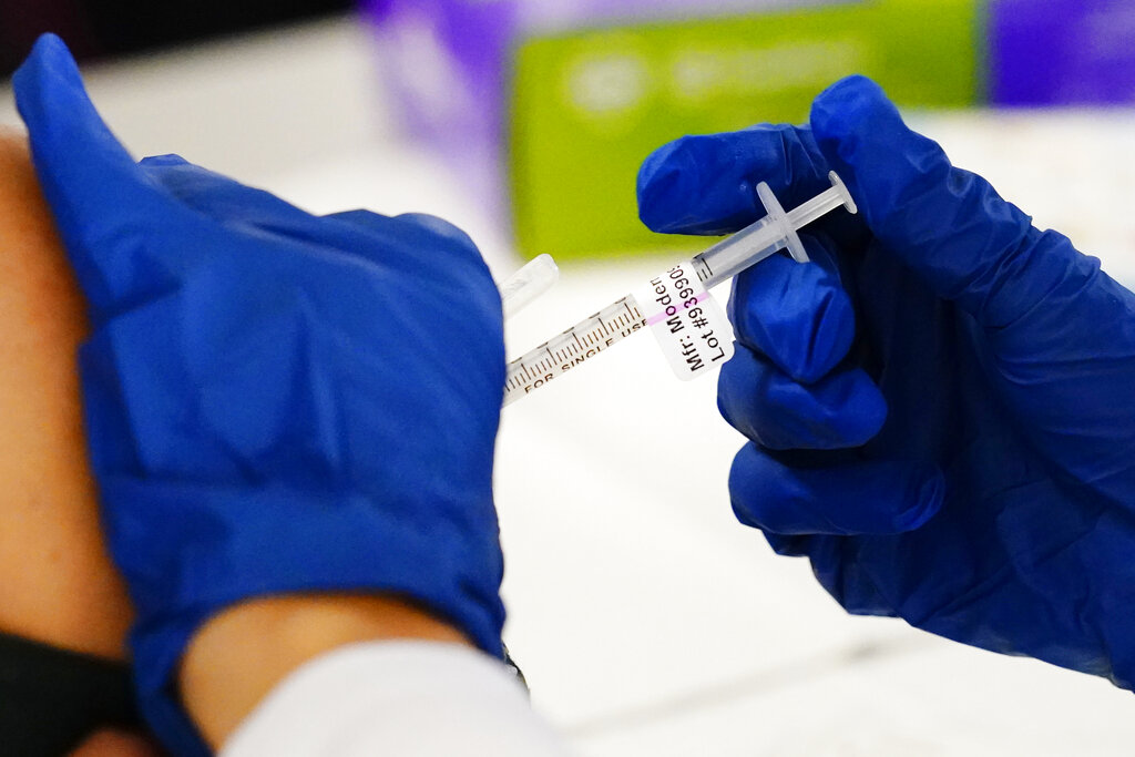 Wearing rubber gloves and using a syringe, a health worker administers a dose of a Moderna COVID-19 vaccine at a vaccination clinic in Norristown, Pennsylvania.