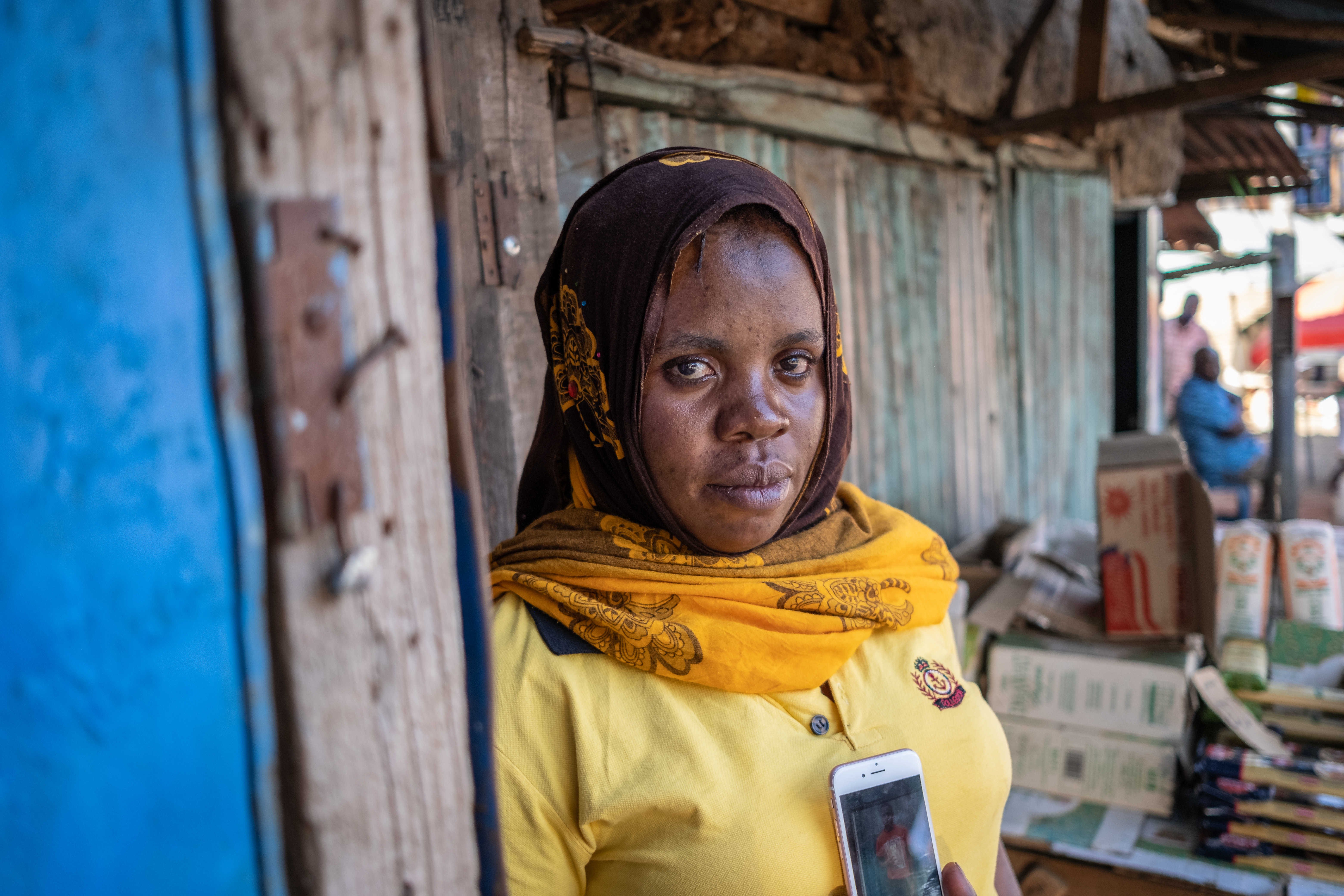 A photo of Rukia Shaban holding a cellphone displaying a photo of her son Ramadhan Bakari.