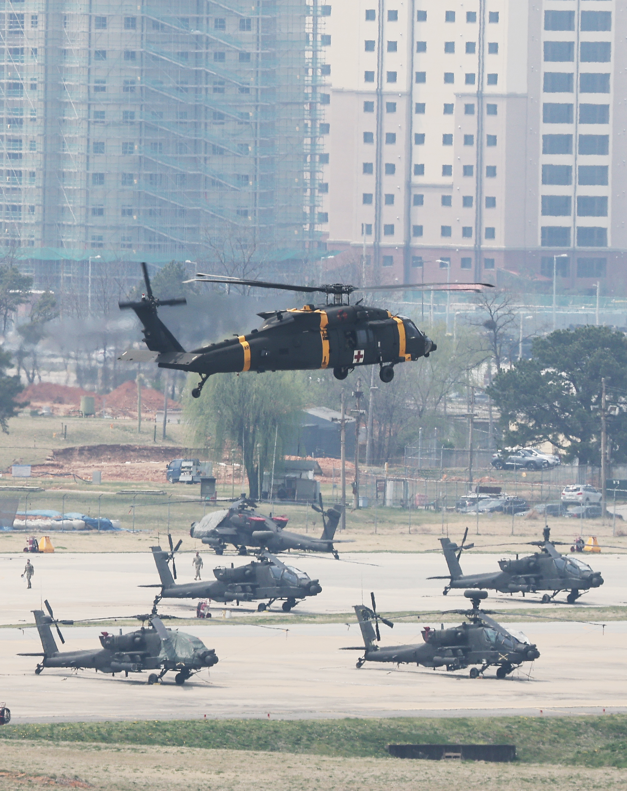Military helicopters in the air and on the ground at US Army base Camp Humphreys with residential tower blocks behind