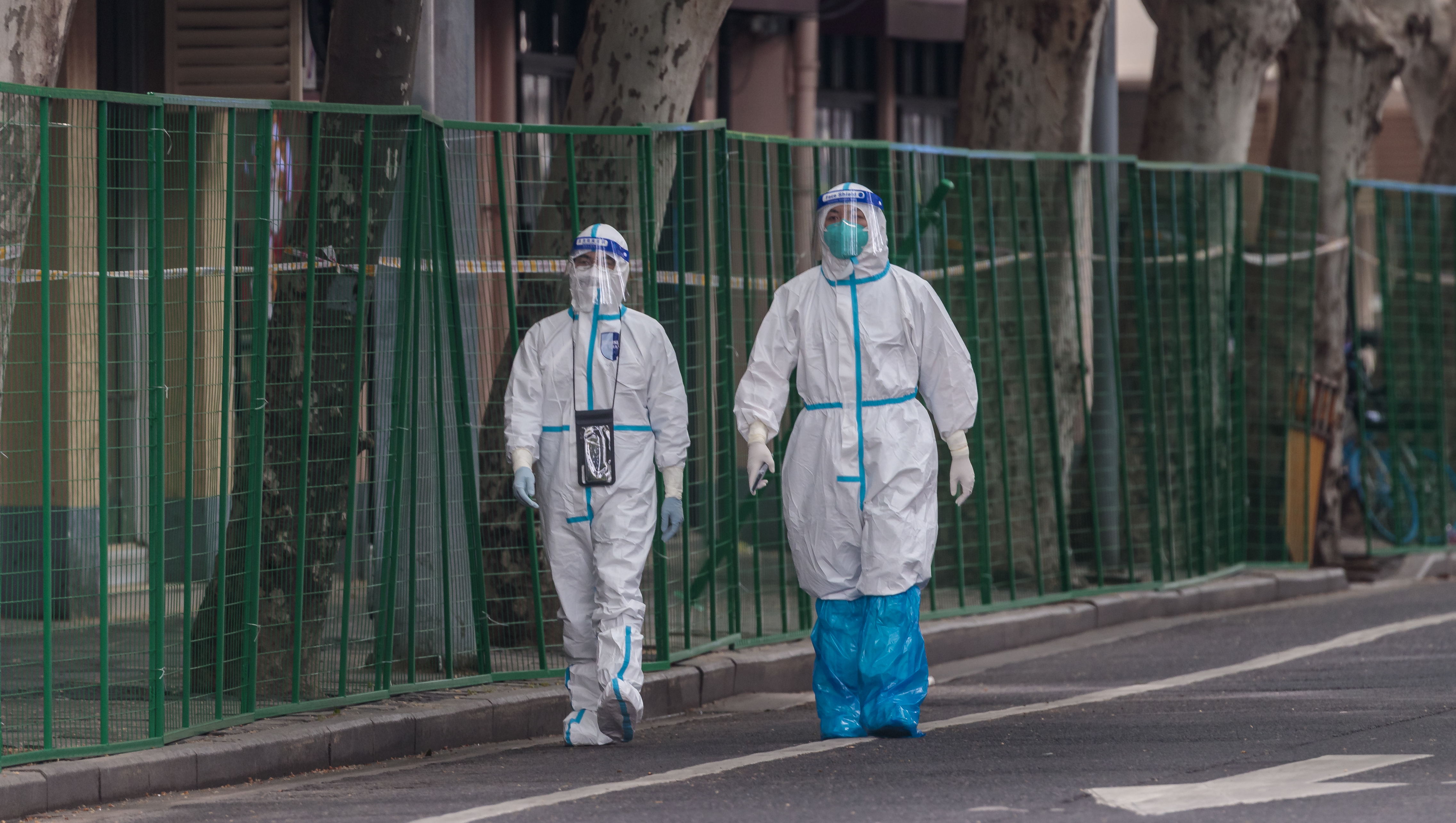 Police in protective gear walk in front of a wire fence recently installed to seal off a quarantined residential compound.