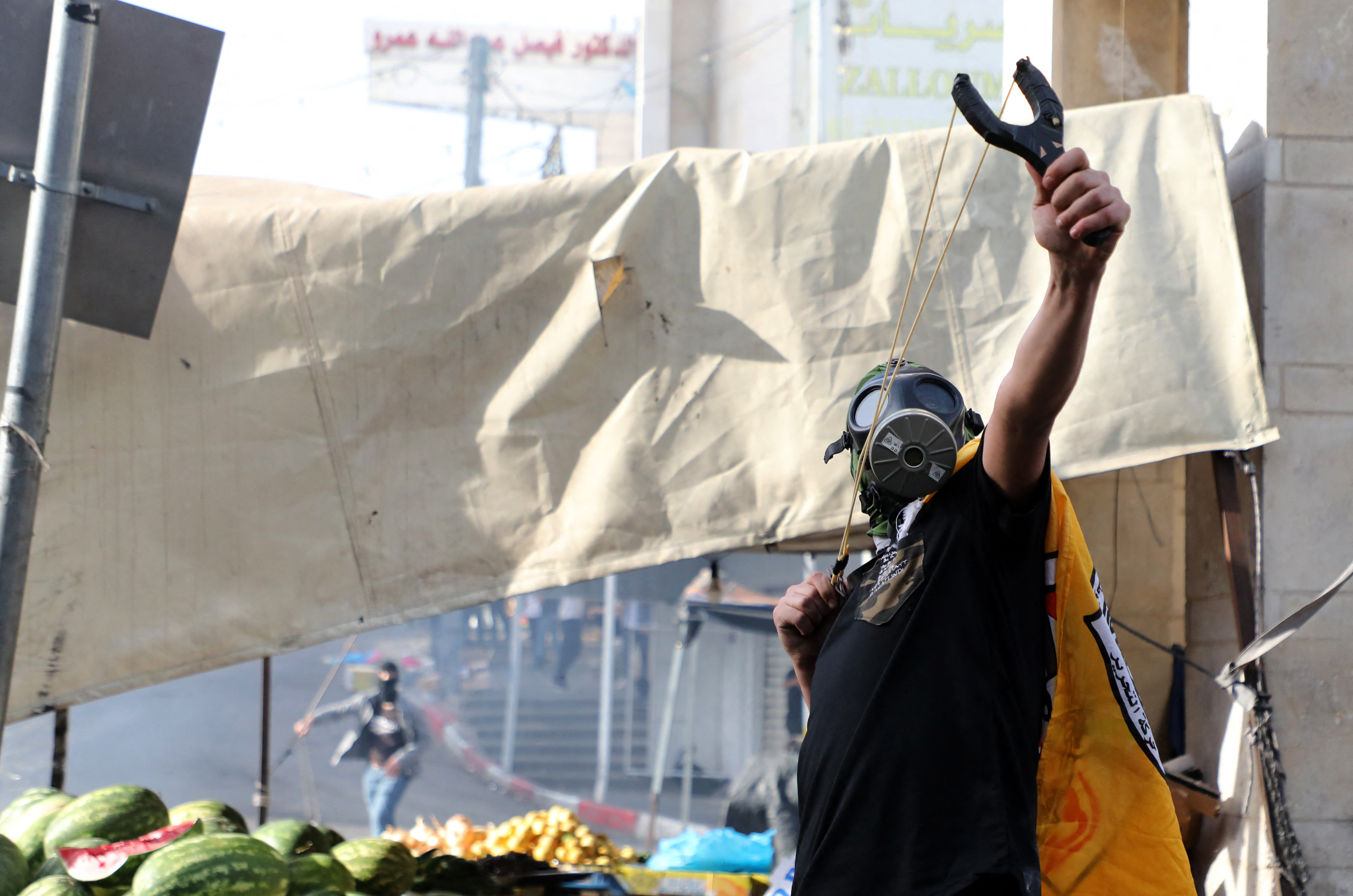 A Palestinian protester wearing a gas mask uses a slingshot to fire rocks at Israeli forces during clashes following a demonstration to denounce the annual nationalist 'flag march' through Jerusalem, in the city of Hebron in the occupied West Bank