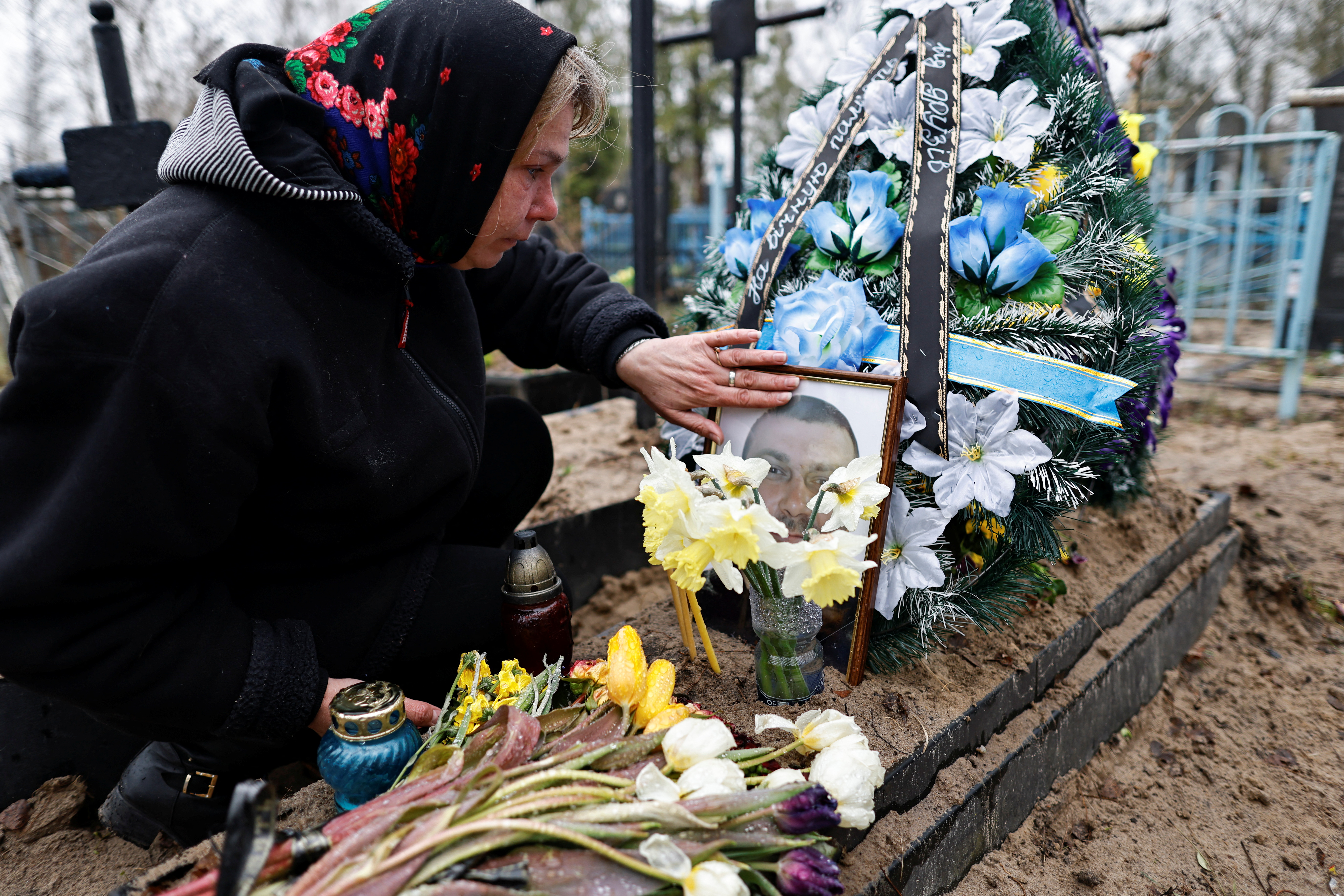 A resident of Bucha touches a framed photo on the grave of her husband.
