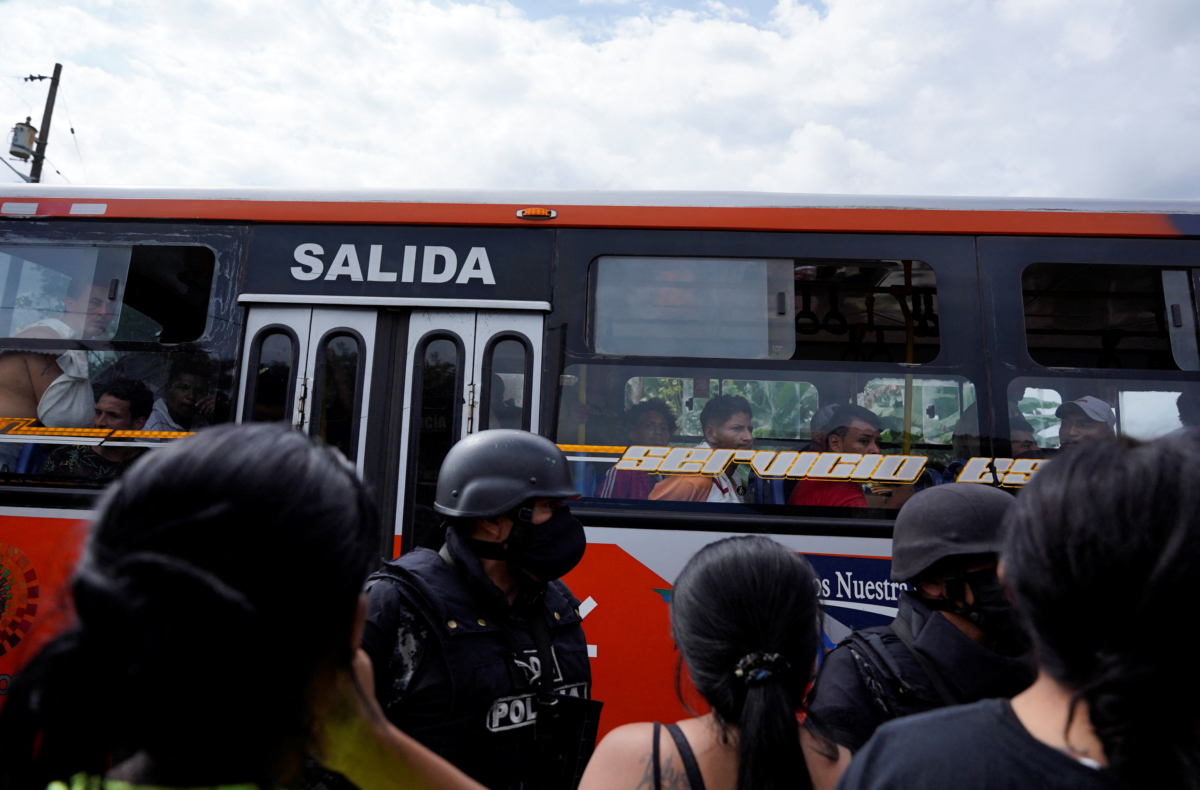 Family members look as a bus passes carrying prisoners