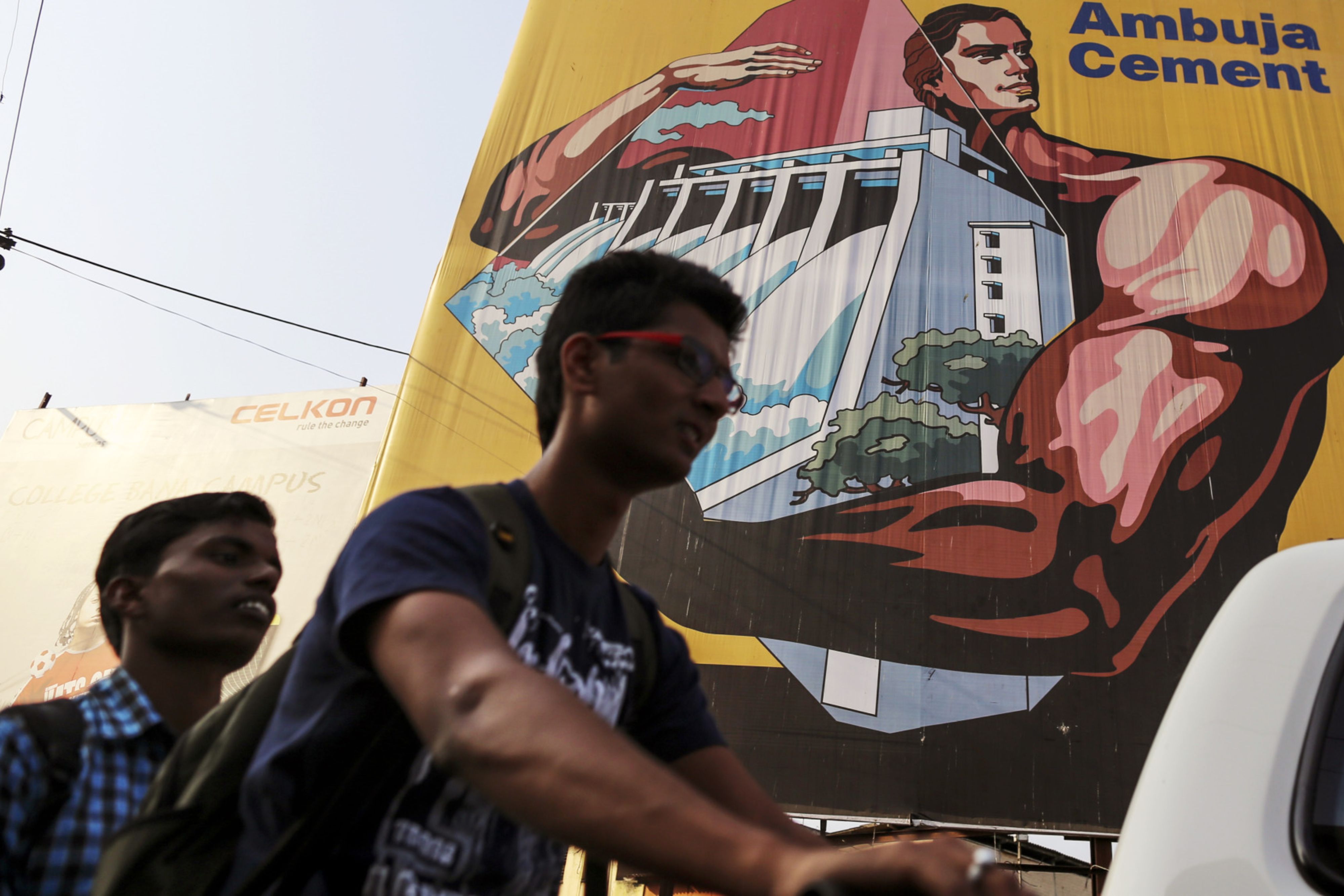 Men on a motorbike pass by an advertisement for Ambuja Cements in Maharashtra, India