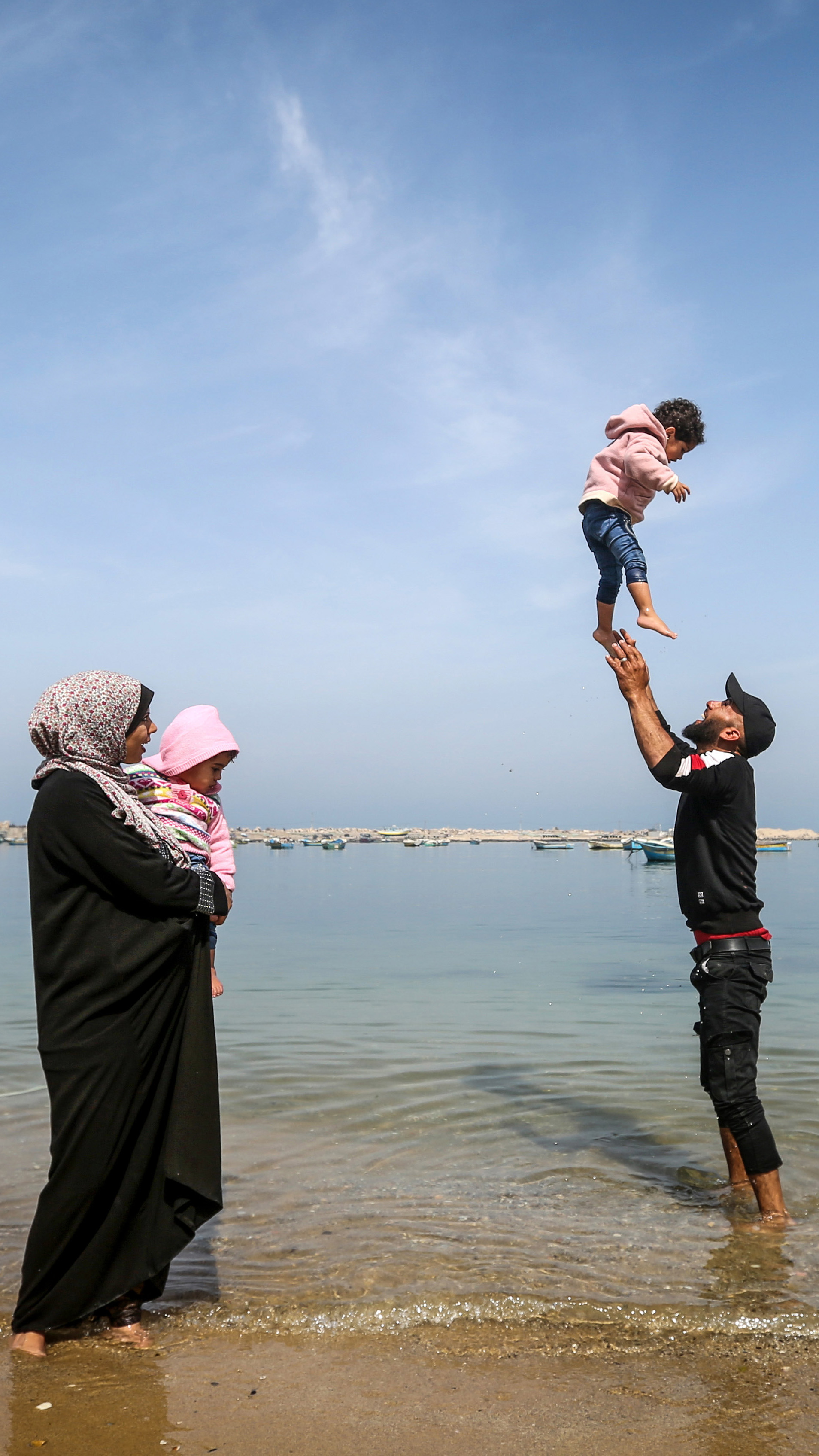 At the water's edge, Khadr plays with Sandy as Madelyn stands by holding Safinaz