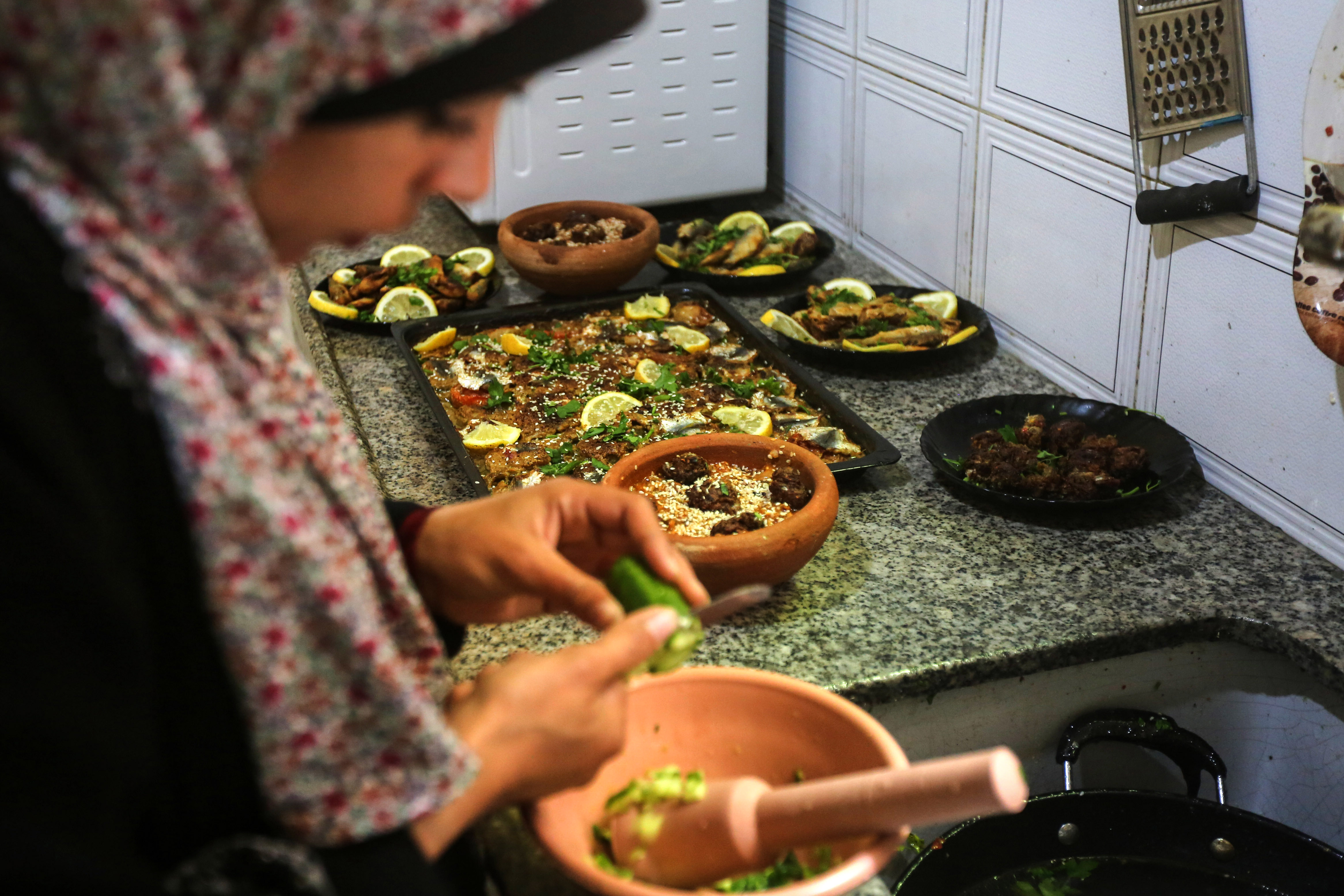Madelyn is in the foreground chopping vegetables into a mortar while in the background dishes for the meal are laid out on the counter