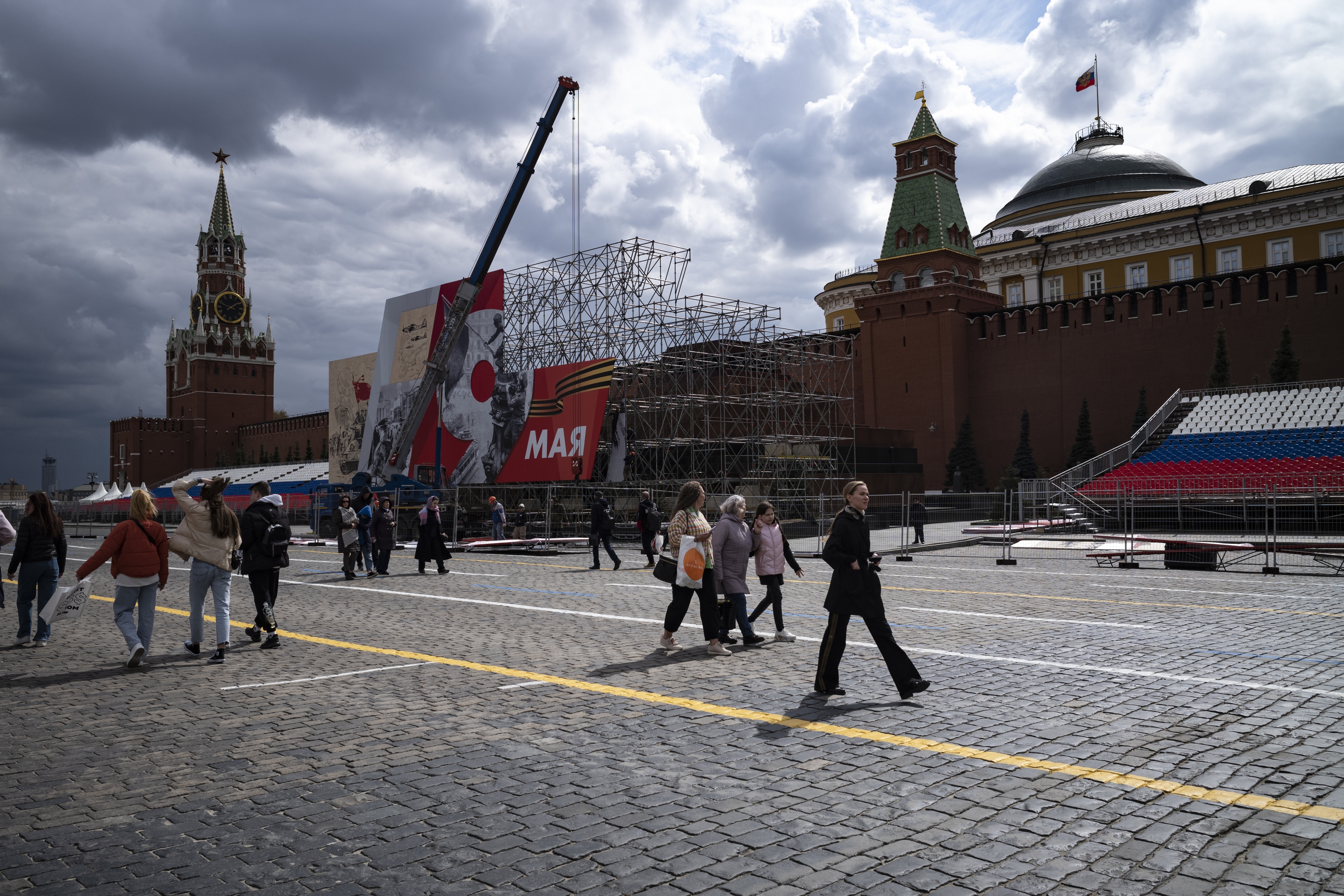People walk in Red Square where municipal workers install decorations for the celebration of Victory Day in Moscow, Russia.