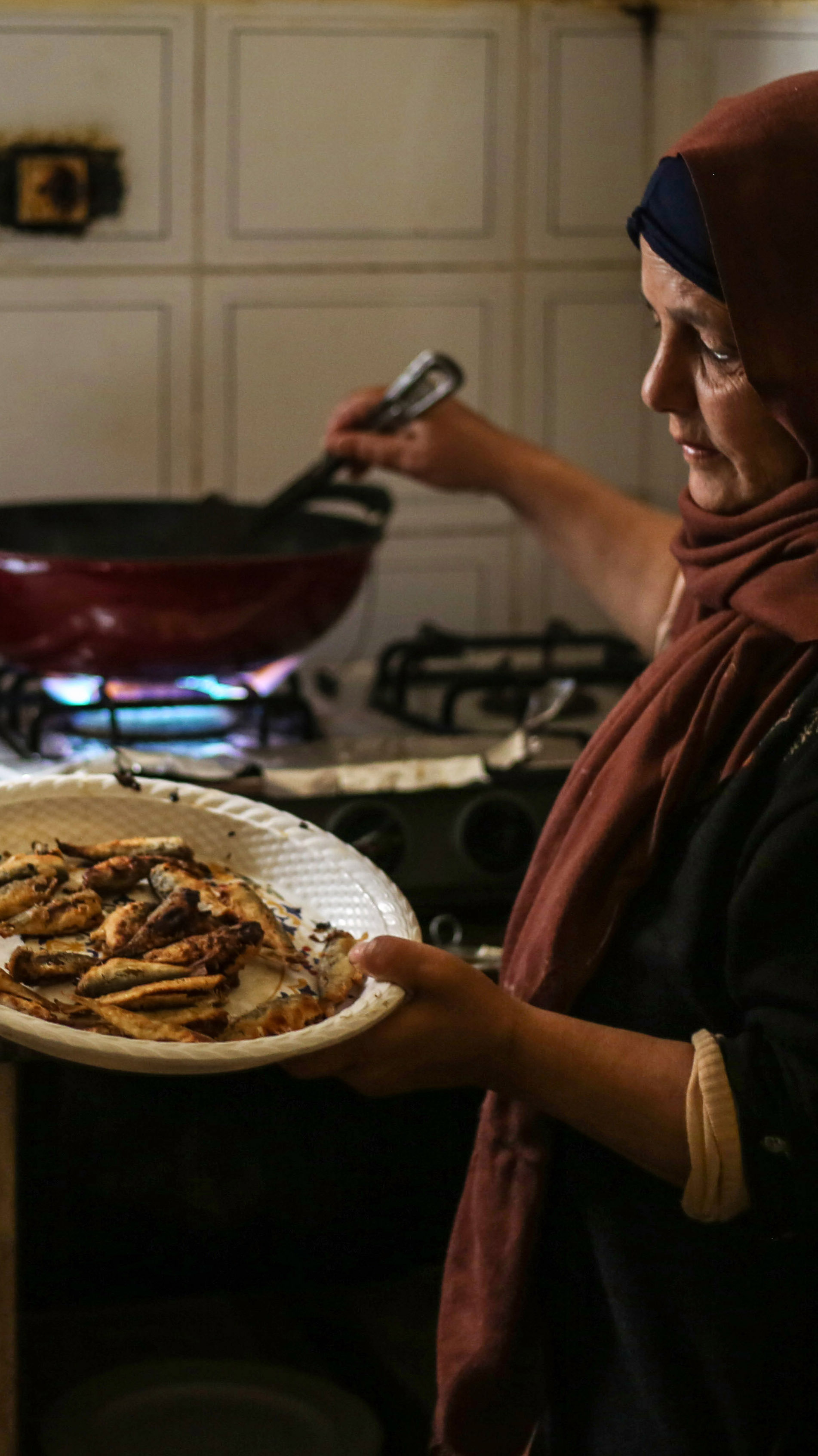 Khadr's mother stands by the stove lifting hot, freshly fried sardines out of a wok and onto a plate