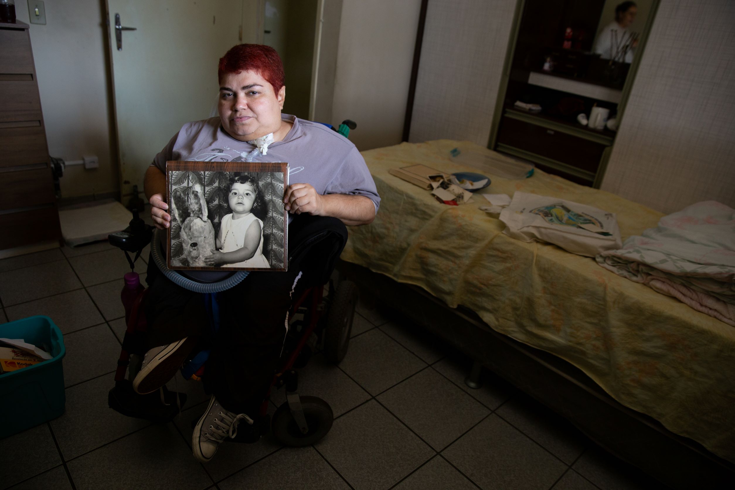 Polio survivor Eliana Gonçalves poses for a portrait with photos of herself as a child