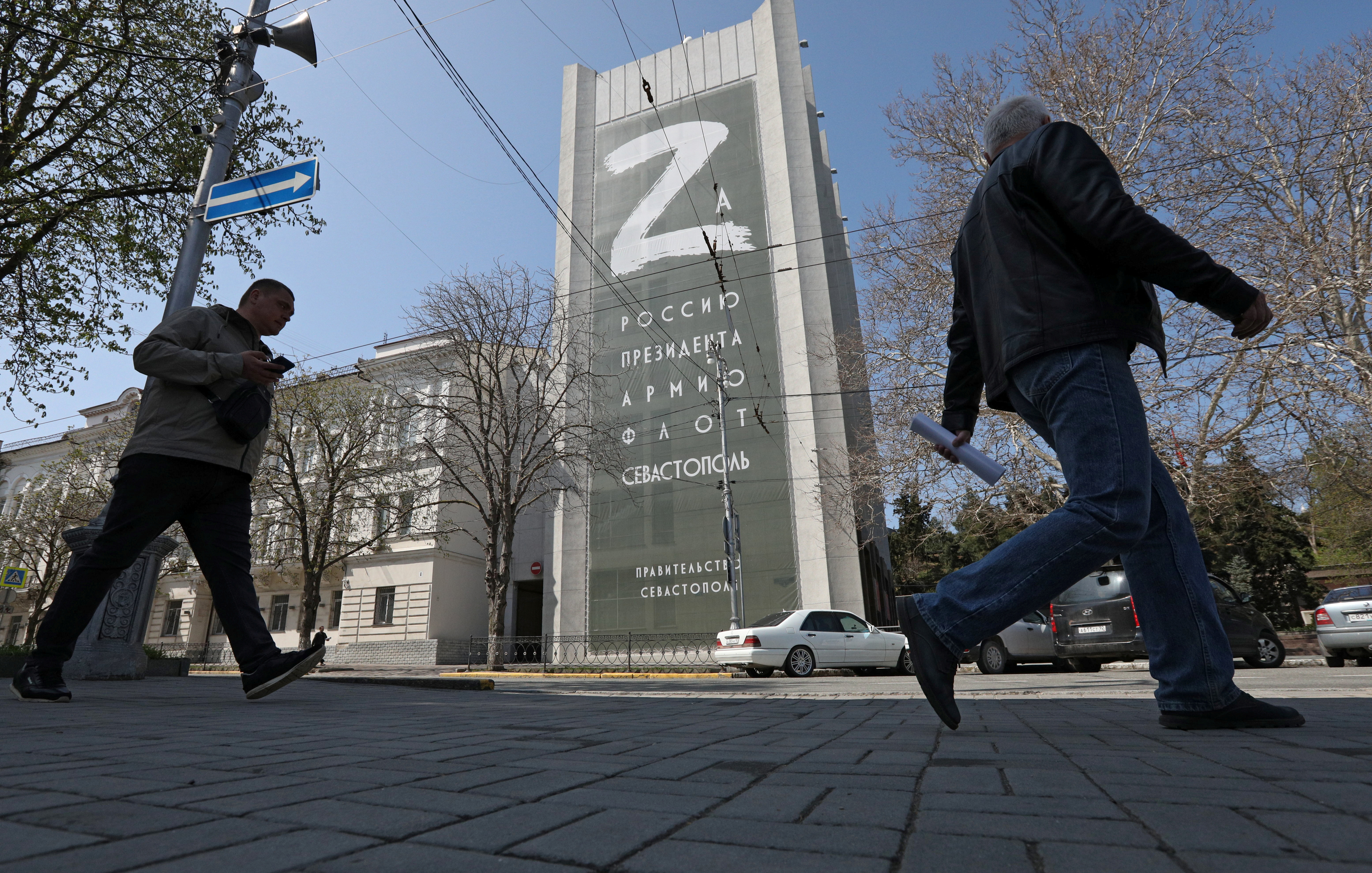 People walk past a banner displaying the "Z" symbol, which Russian armed forces use as a motif in Ukraine, in Sevastopol, Crimea April 15, 2022. The banner reads: "For Russia, the president, the army, the navy, Sevastopol." 