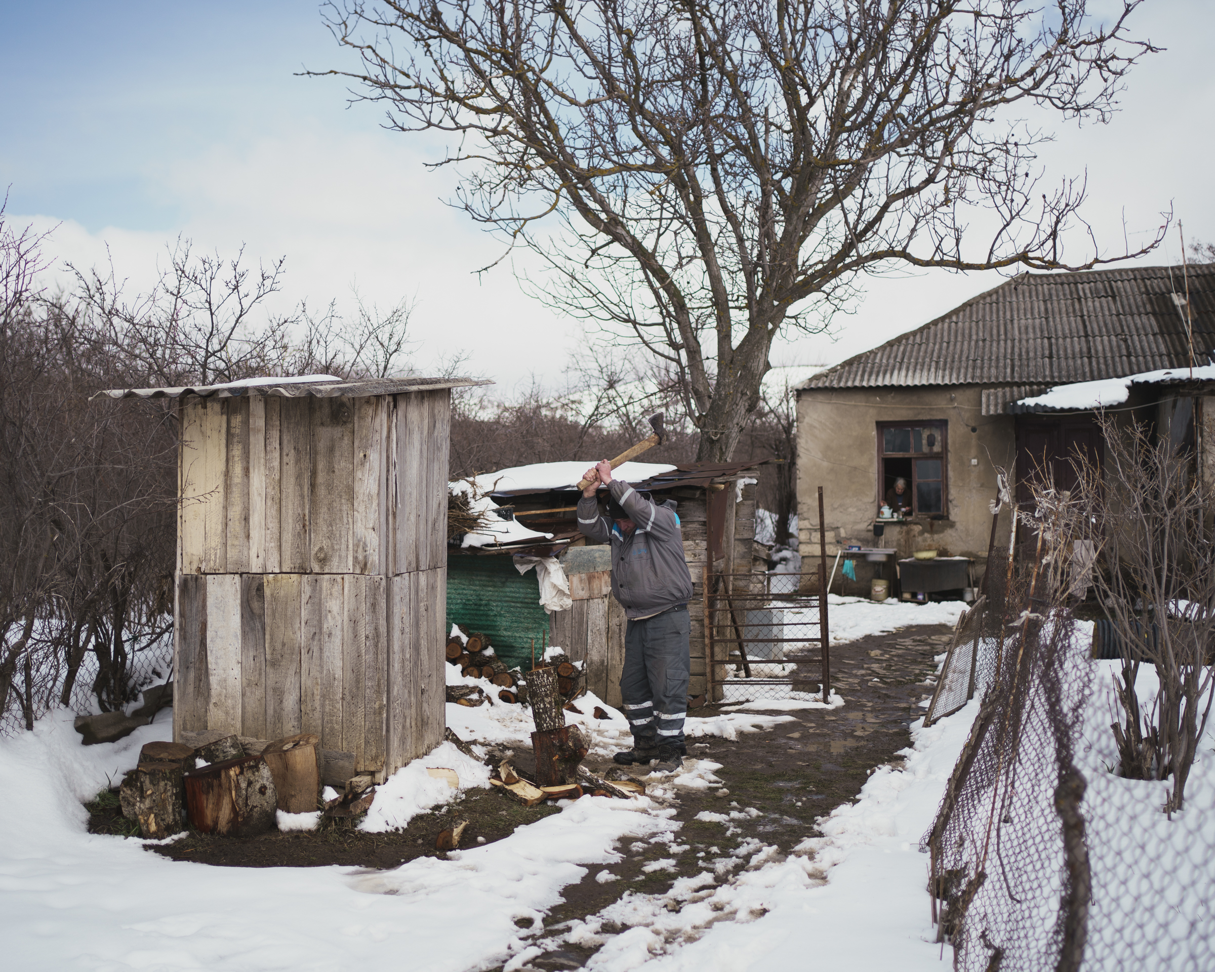 A photo of a person chopping wood outdoors in the snow.