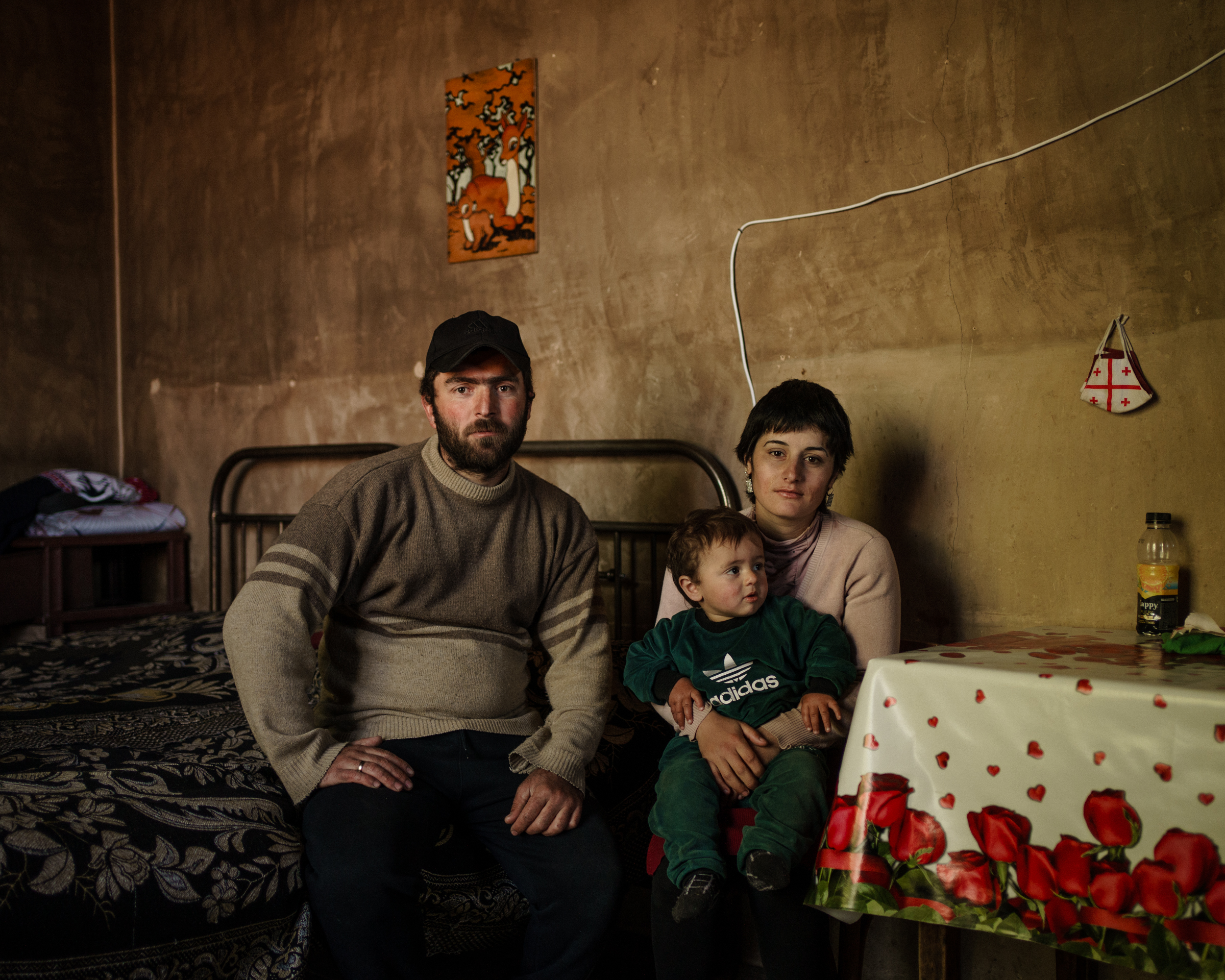 A photo of a family of three, a man on the left and a woman holding a child on her lap on the right.