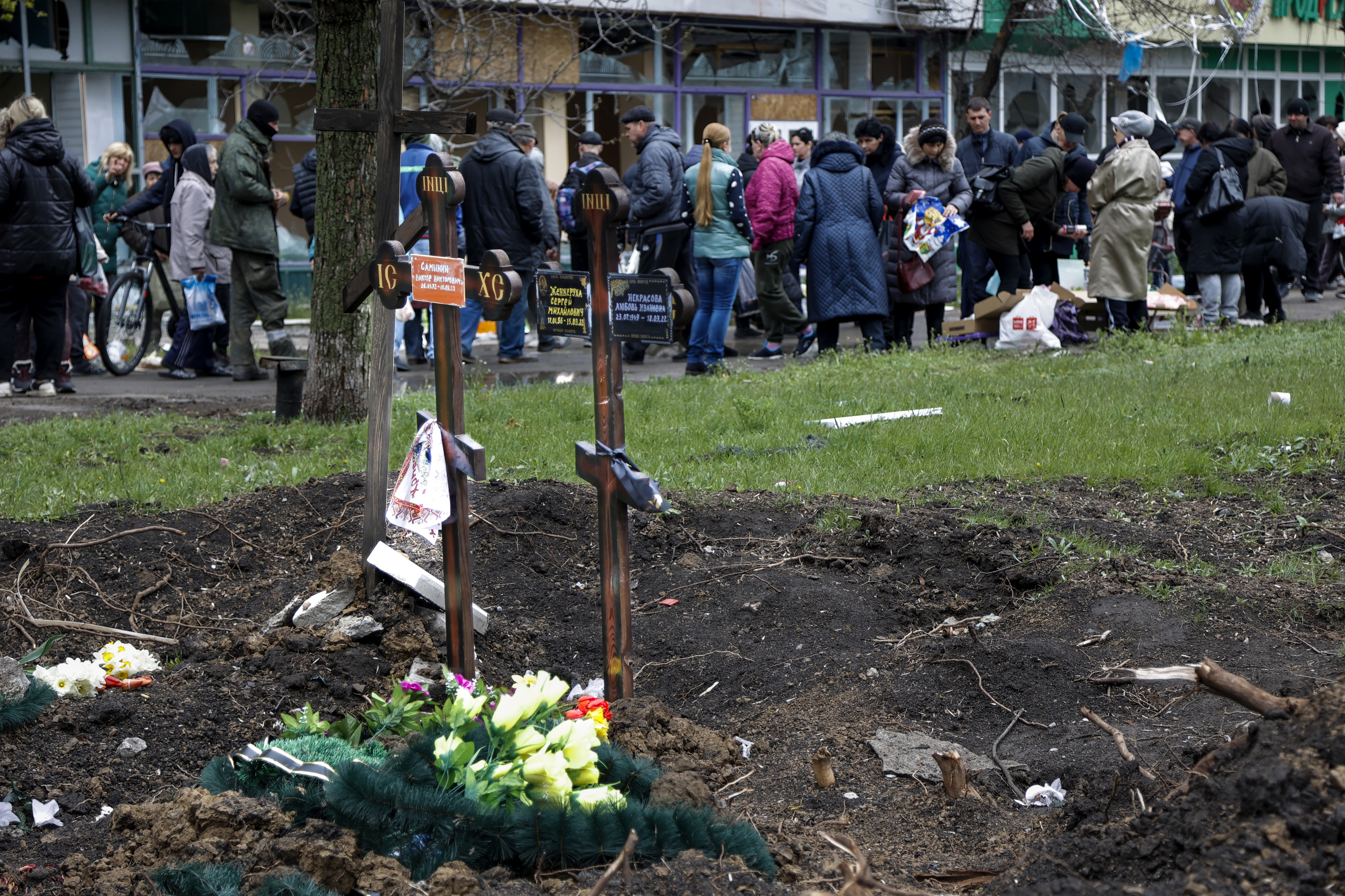Local residents gather at a makeshift street market next two fresh graves in the foreground in an area controlled by Russian-backed separatist forces in Mariupol, Ukraine, Friday, April 22, 2022