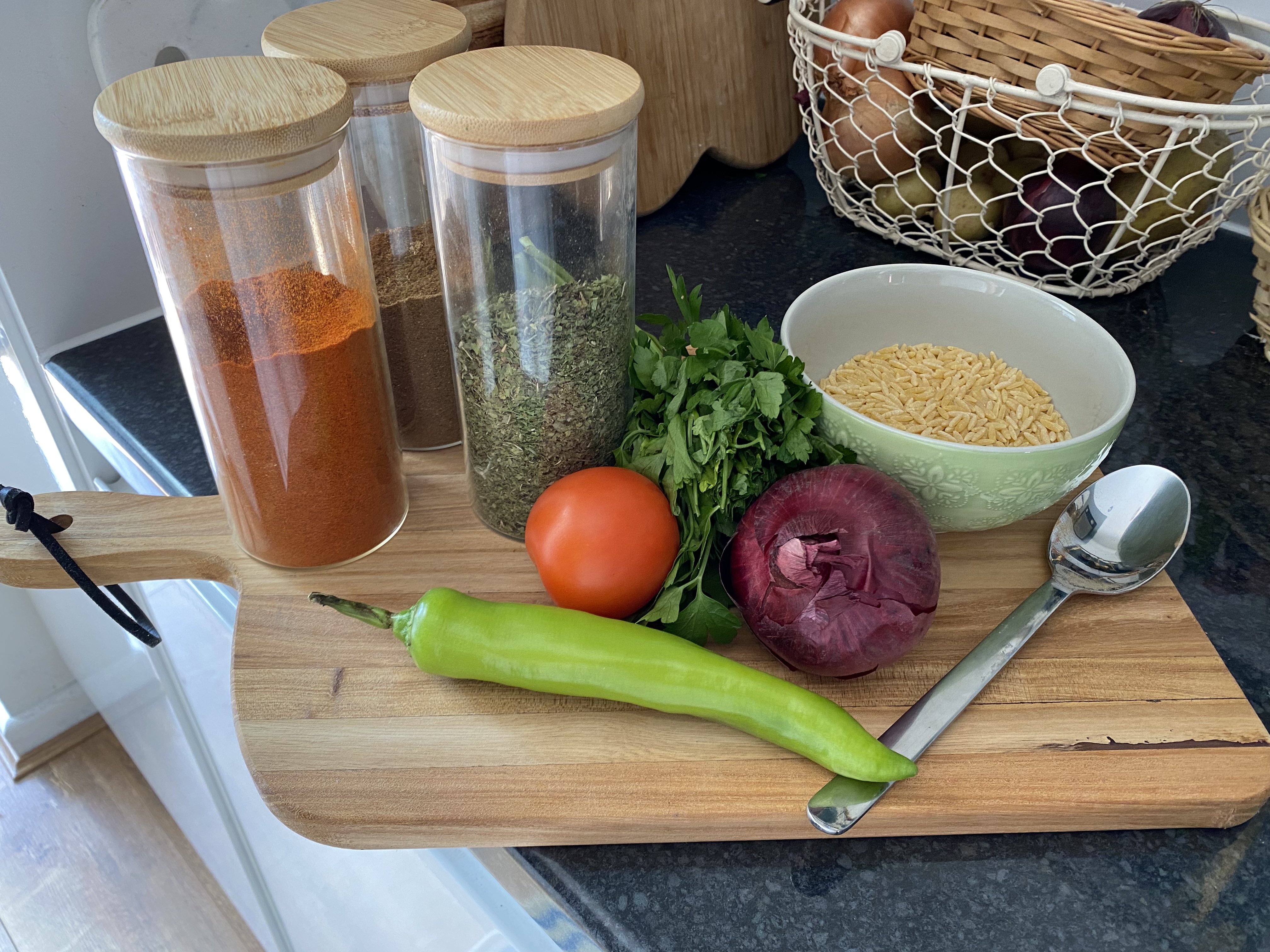 Ingredients are gathered on a wooden cutting board. Onion, tomaro, rice, spices