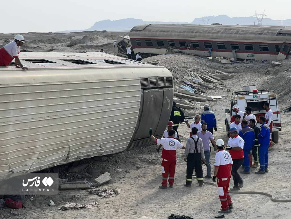 A group of people stand next to a derailed train