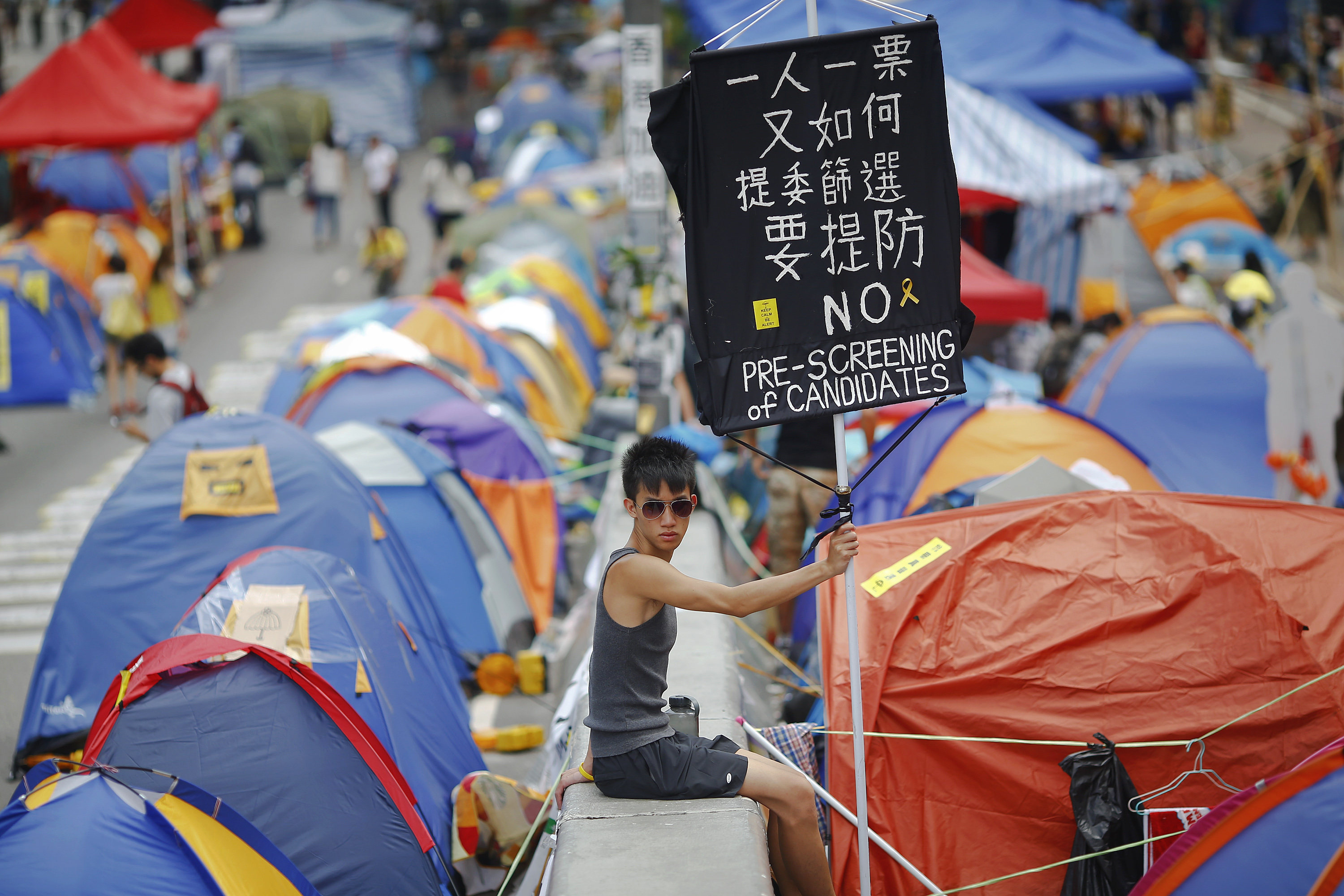 A pro-democracy protester holds a banner with tents set up on the street around him. 