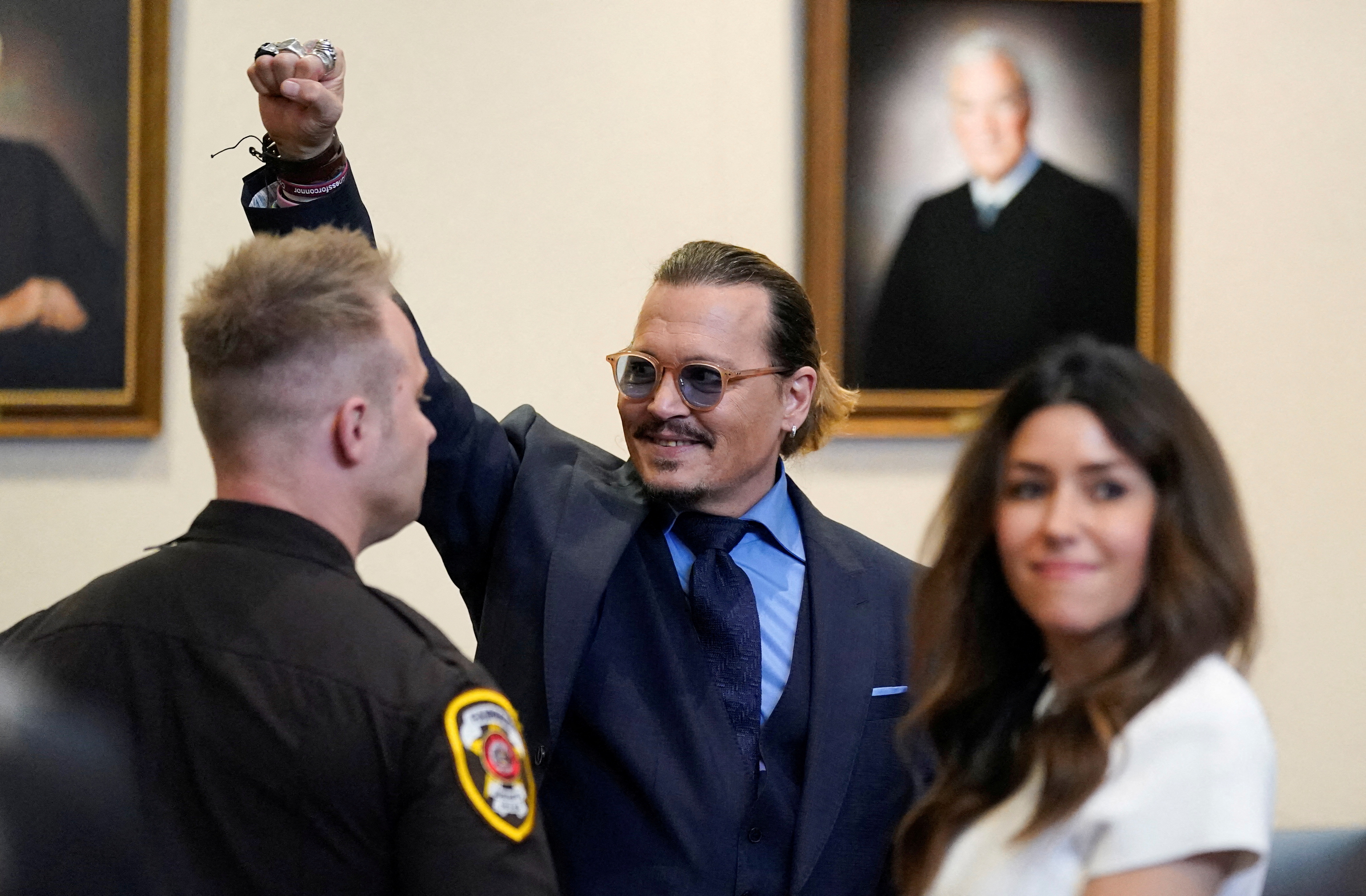 Johnny Depp, with his lawyer to his left and a court security guard to his right, waves to people in court during his defamation trial against ex-wife Amber Heard