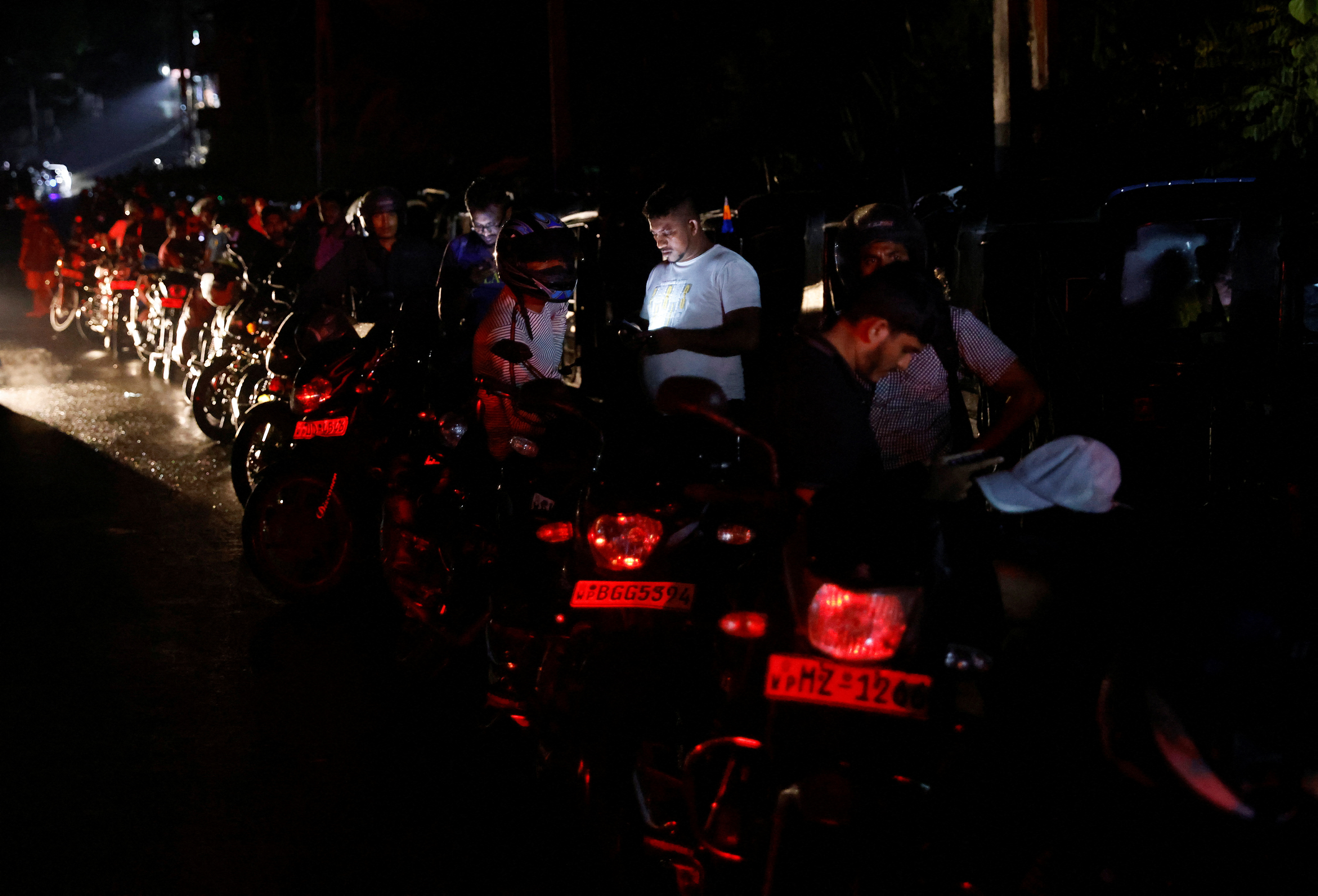 People stand next to their motorbikes as they queue to buy petrol during the early hours of the morning at a fuel station in Gonapola town