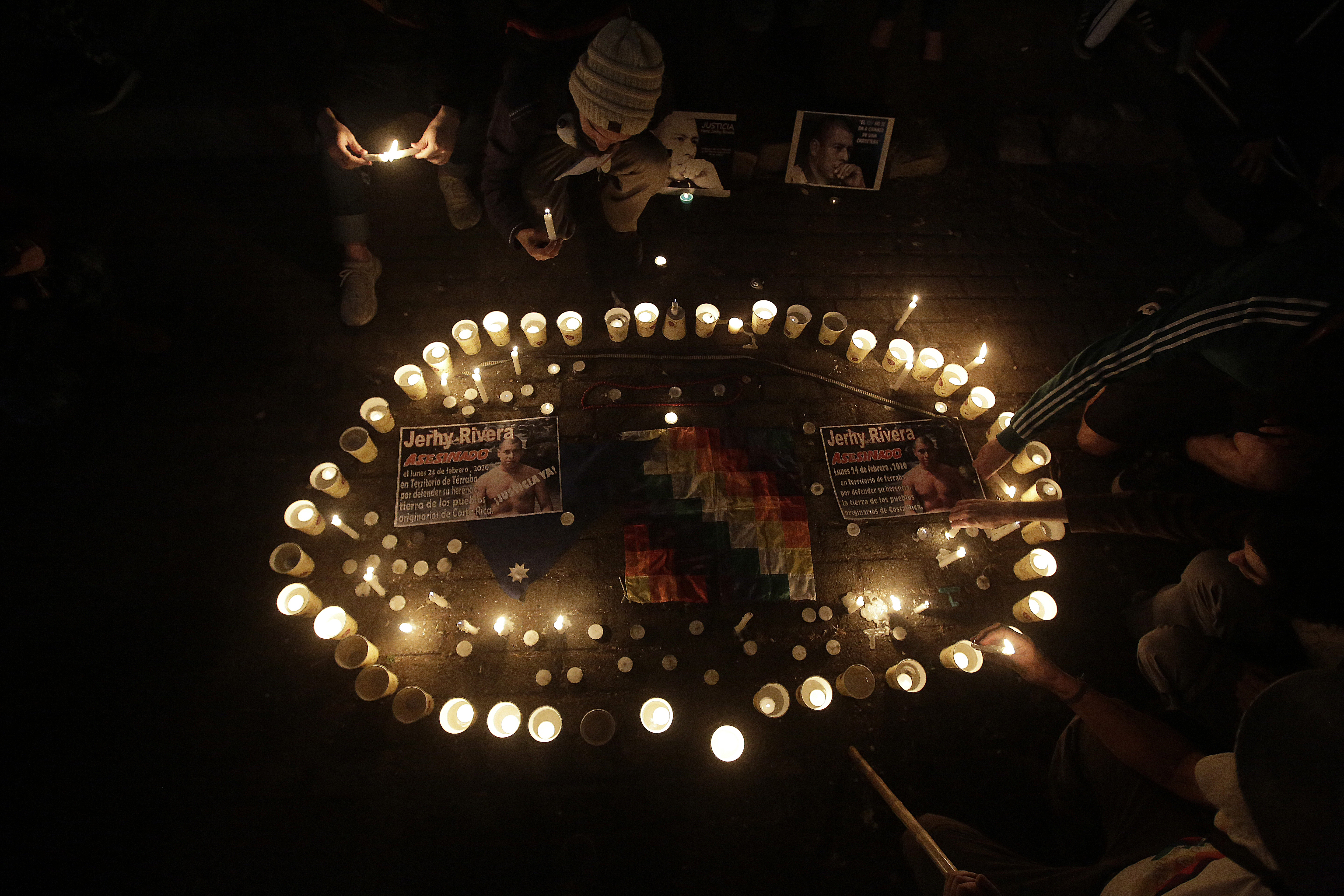 A photo of a vigil held to mourn the death of Jerhy Rivera with a circle of candles with photos of Jerhy Rivera in and around it, with people sitting around the circle..