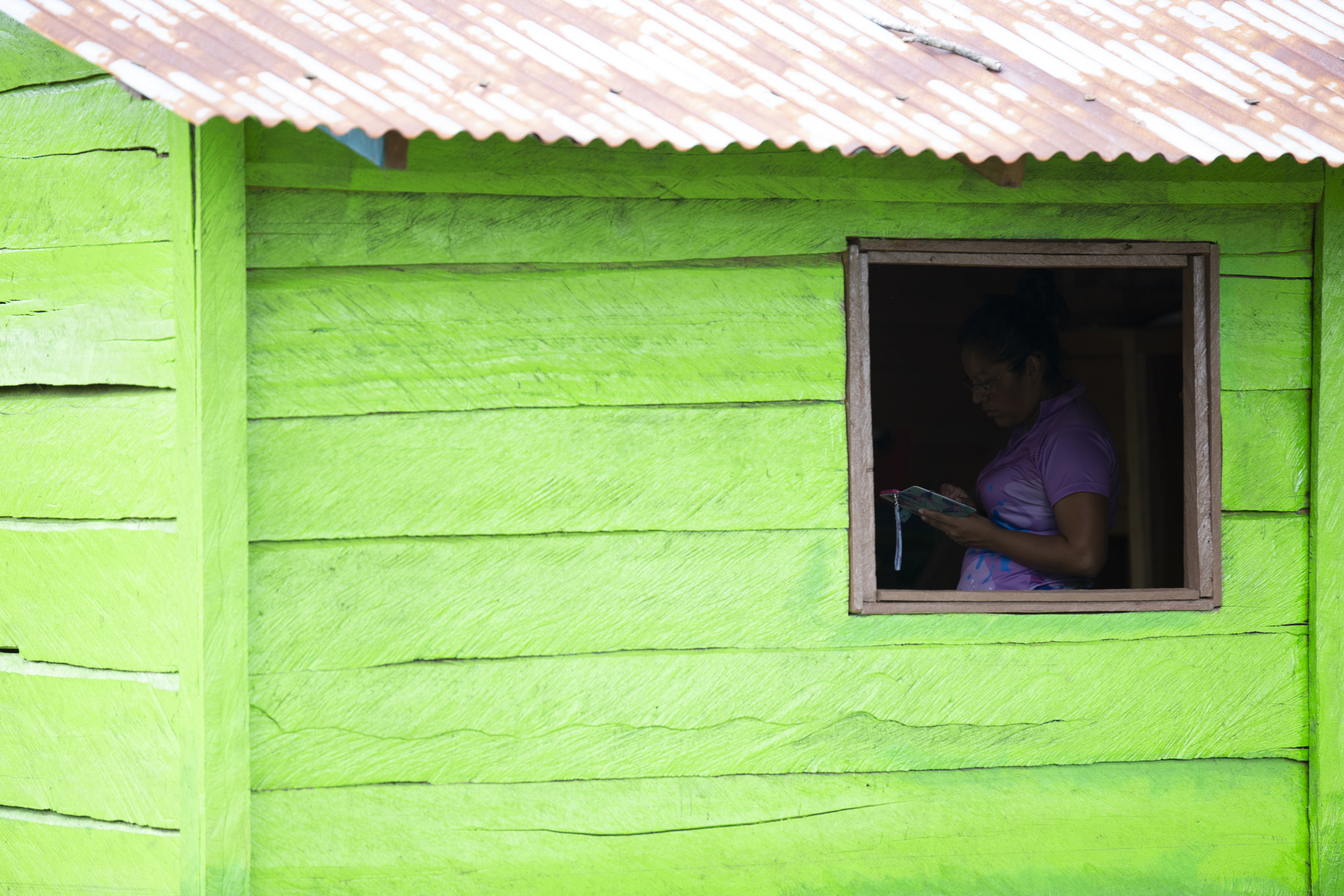 A photo of a green building with a person standing inside looking at their phone.