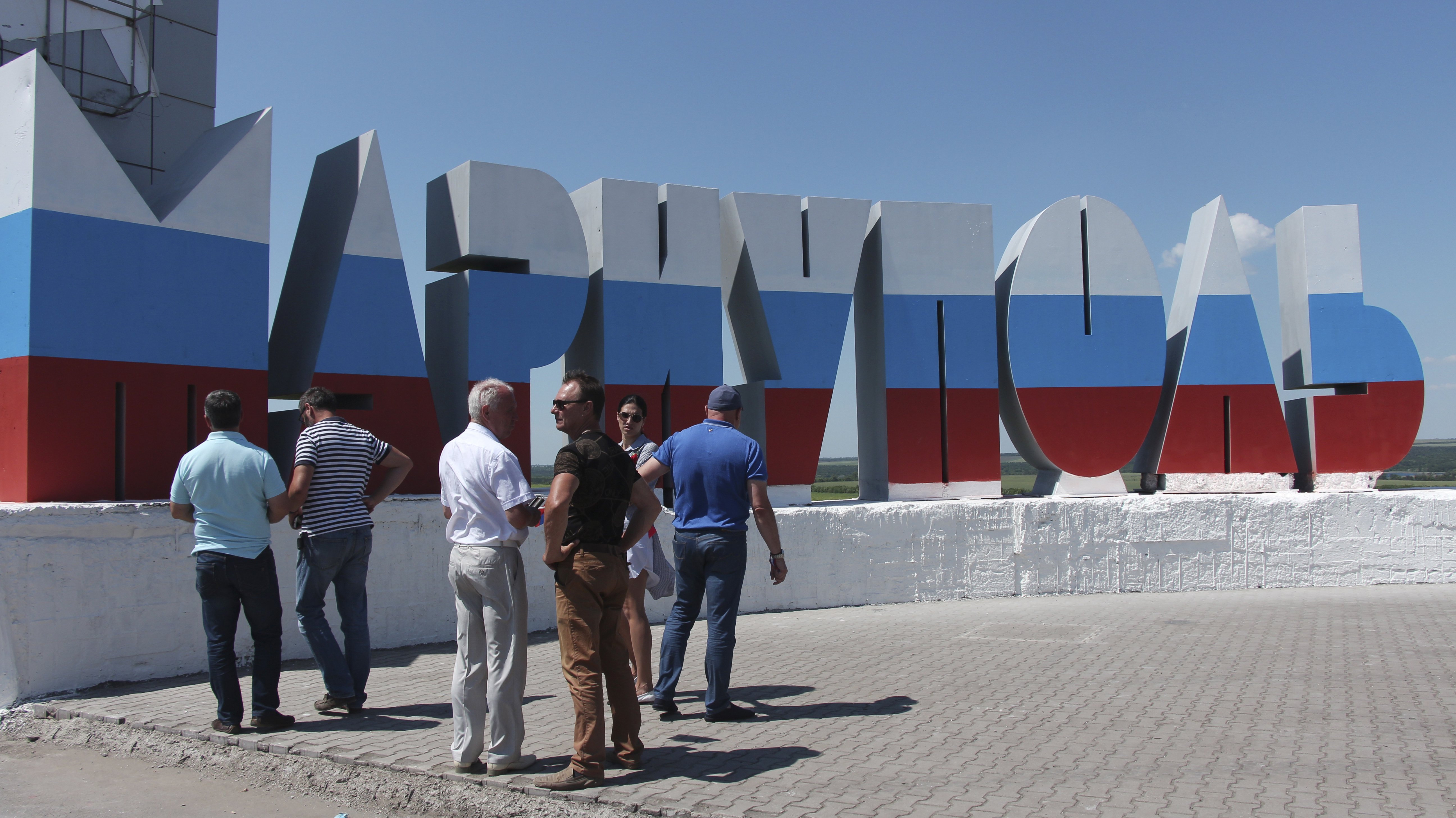 People stand near the name of the city of Mariupol written in Russian and painted in the colours of the Russian national flag during celebration of Russia Day in Mariupol, June 12, 2022