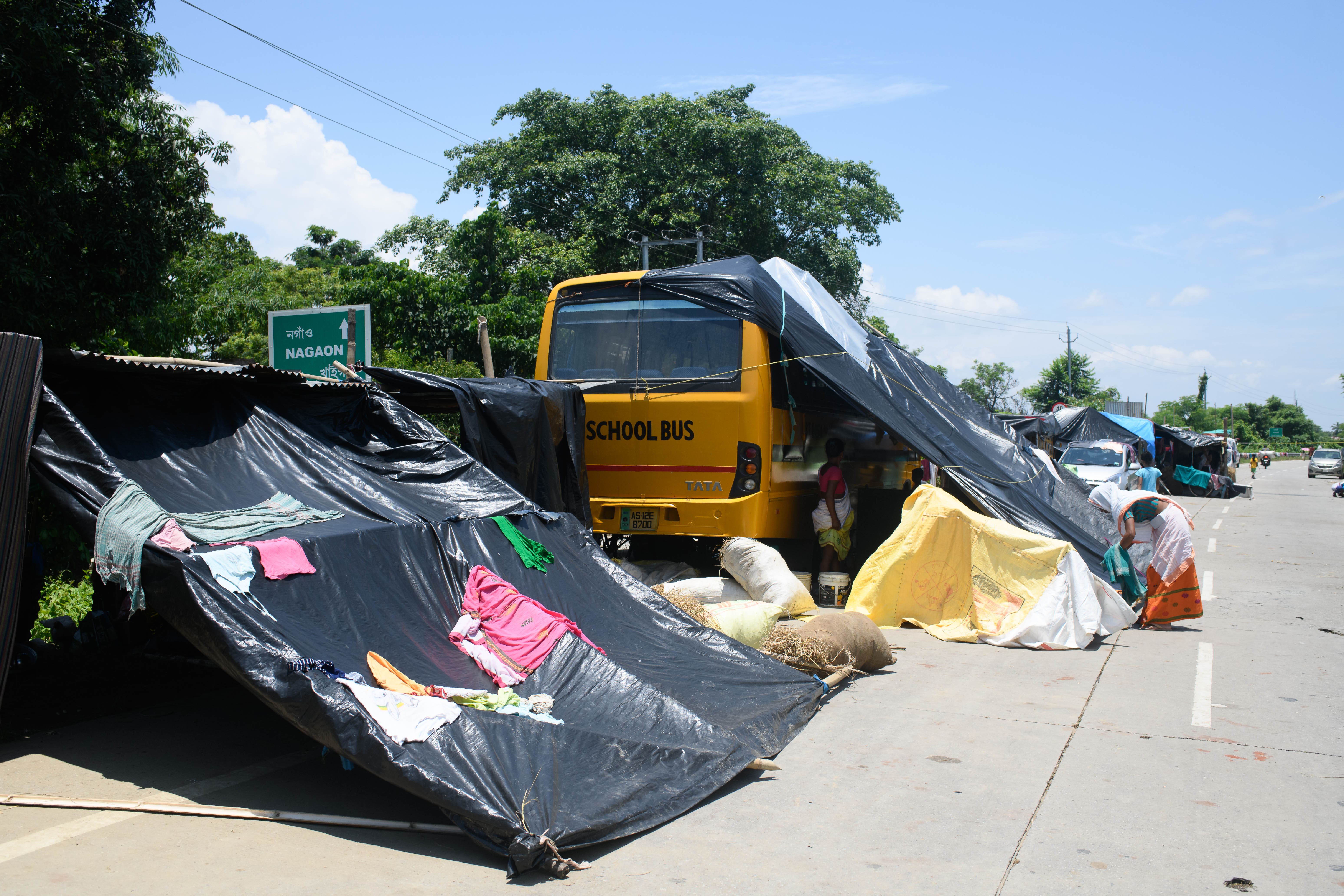 Residents of a flood relief camp uses a school bus to set up a makeshift tent in Raha, Assam