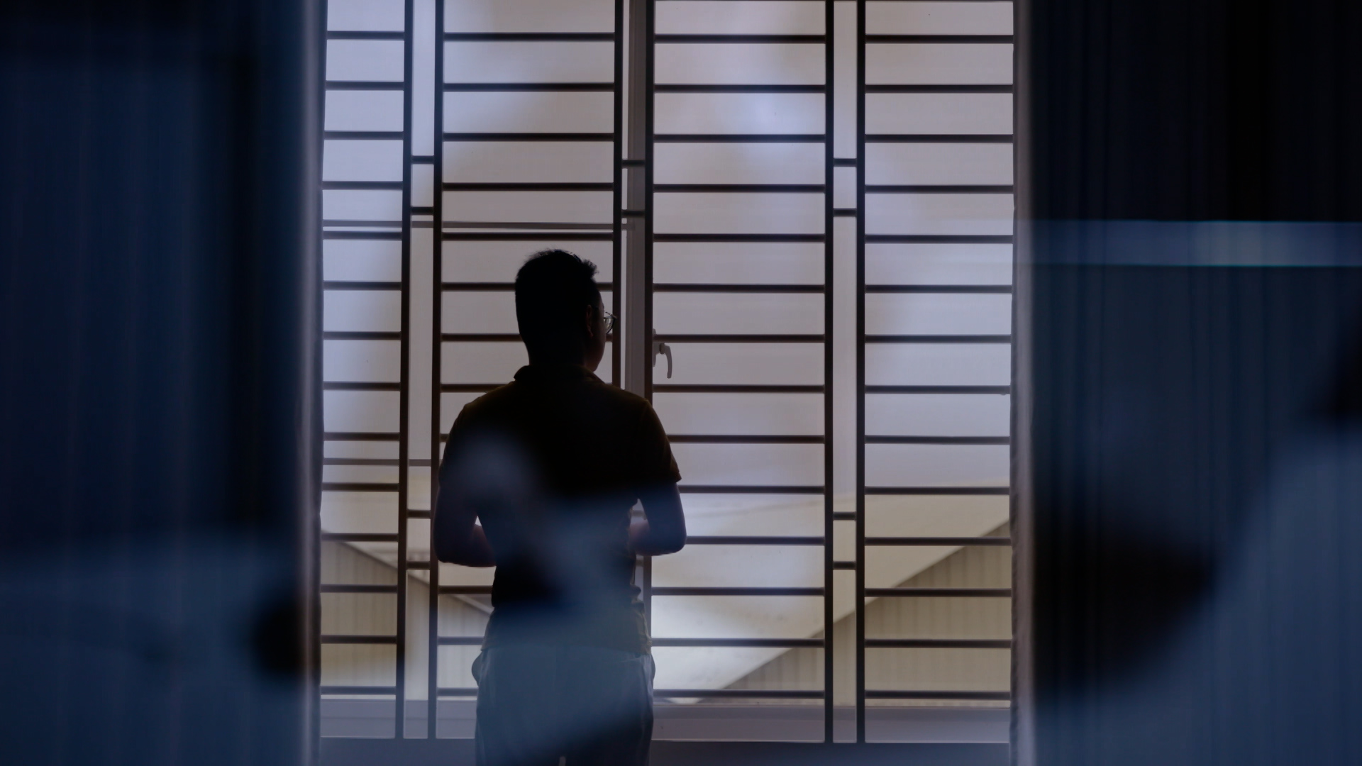 A person in shadow, standing at a window