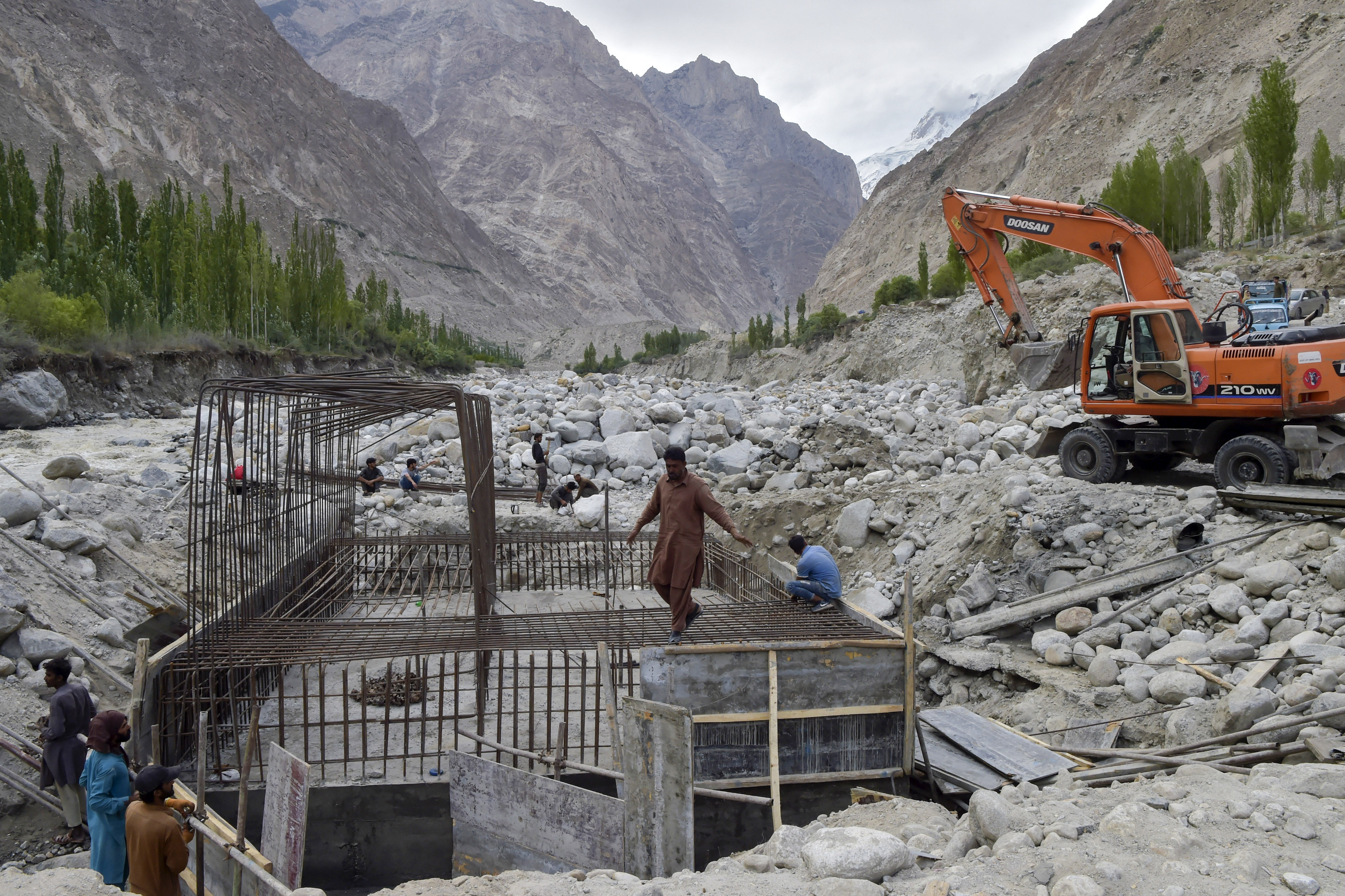 In this picture taken on June 9, 2022, construction workers build a temporary bridge after a lake outburst because of a melting glacier swept away the main bridge in Hassanabad village