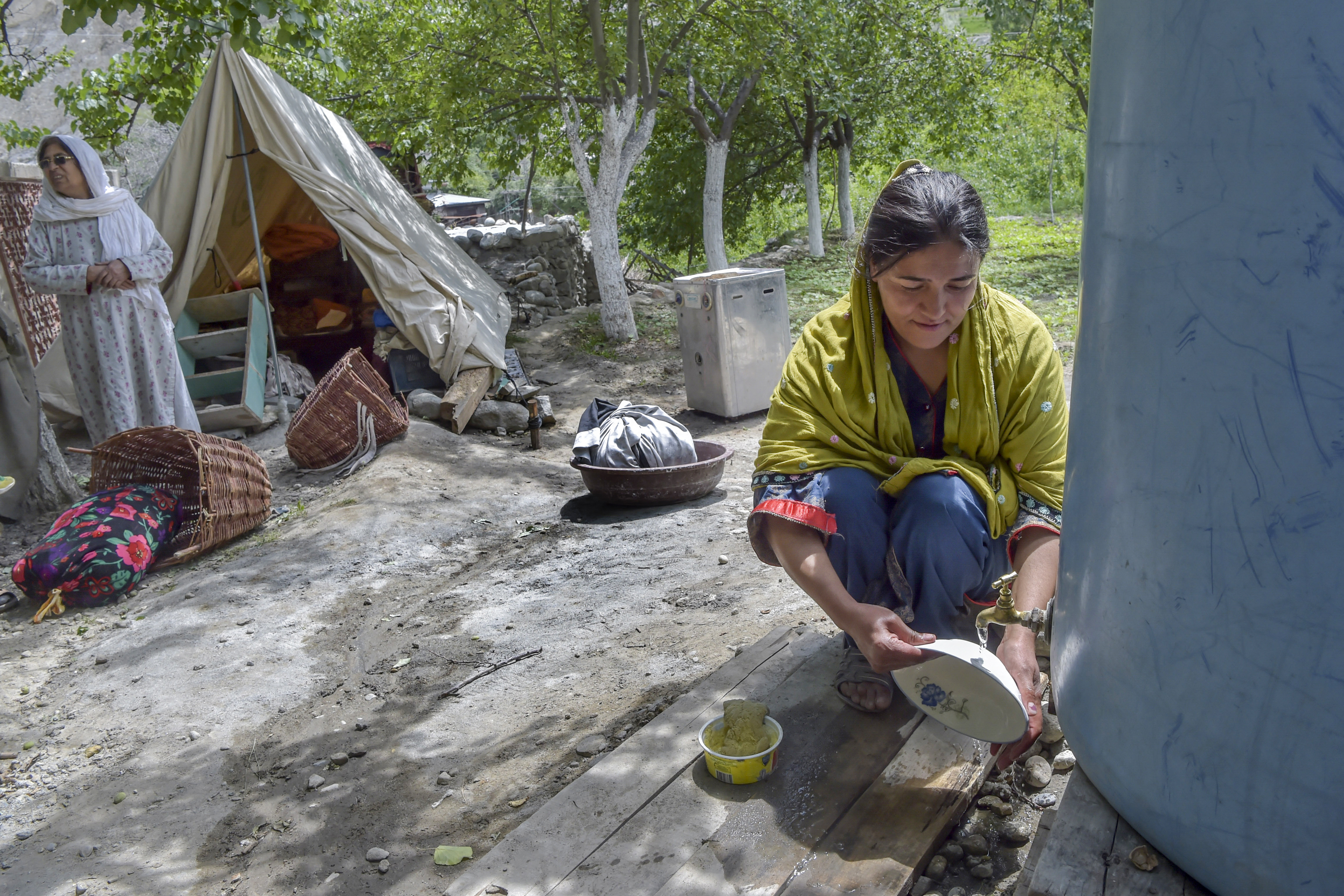 In this picture taken on June 9, 2022, a local resident washes dishes outside tents setup after their homes were swept by a lake outburst because of a melting glacier in Hassanabad