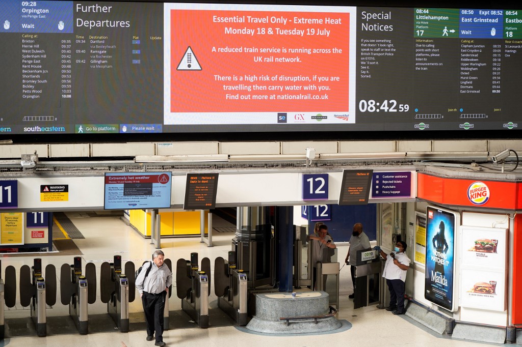 Commuters walk under a message board warning people of disruption over extreme heat at Victoria Station in London