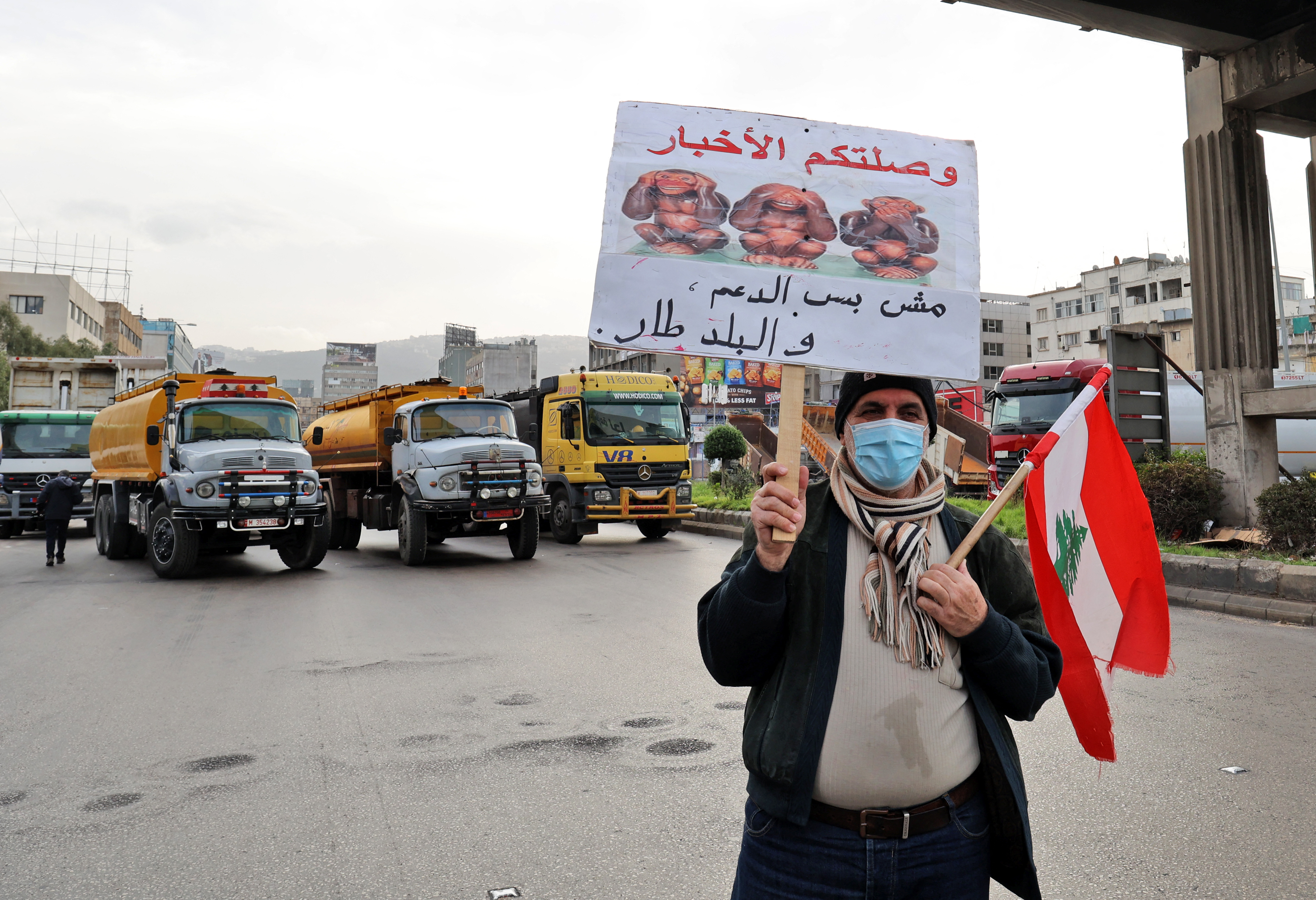 A Lebanese protester holds a sign as fuel tankers block a road in Lebanon's capital Beirut during a general strike by public transport and workers unions
