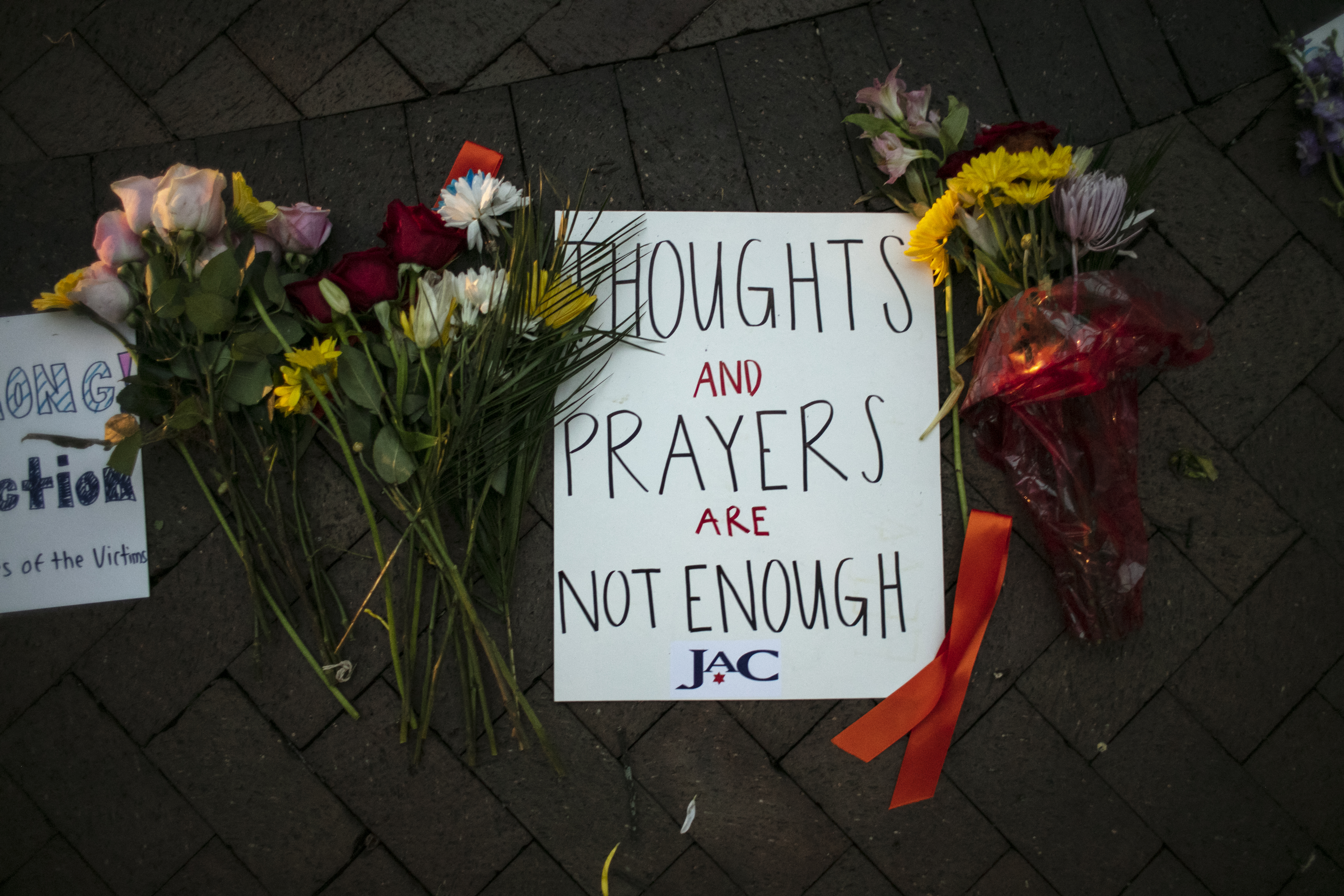 A sign that reads 'Thoughts and prayers are not enough' on the ground with flowers around it at a vigil in Highland Park, Illinois.