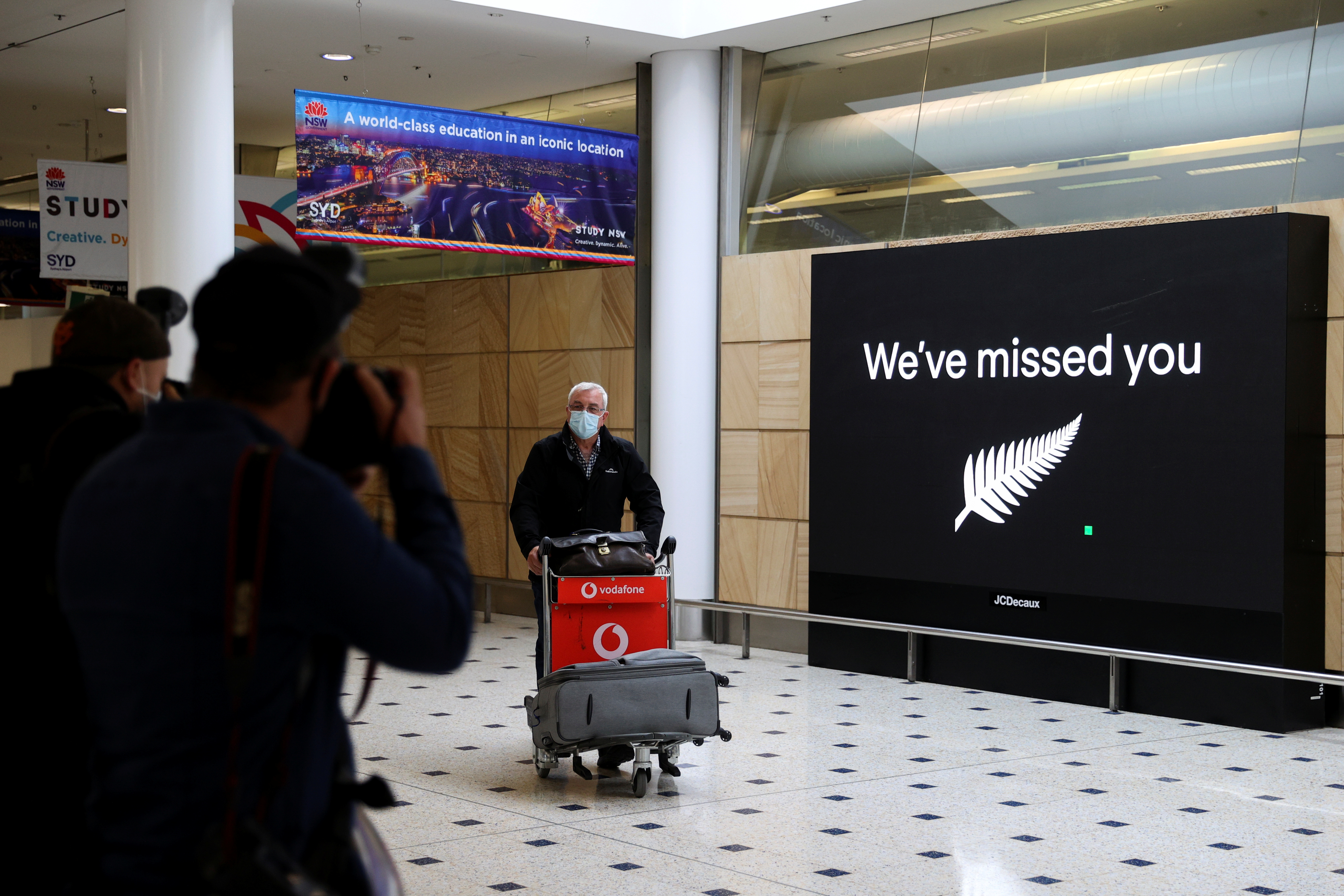 A passenger pushing a trolley full of bagage at the New Zealand airport