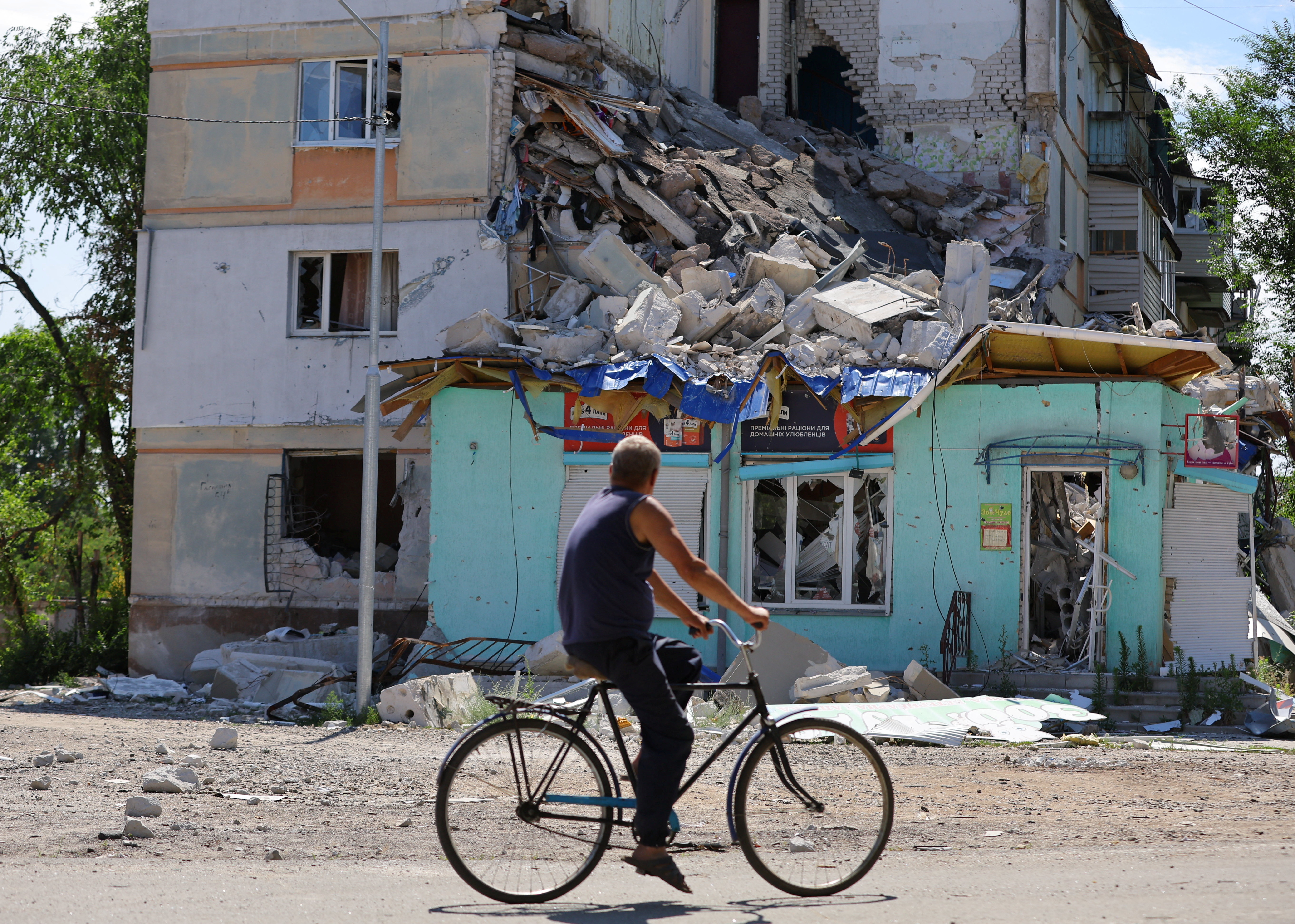 A local resident rides a bicycle past a heavily damaged building in the city of Sievierodonetsk in the Luhansk Region.