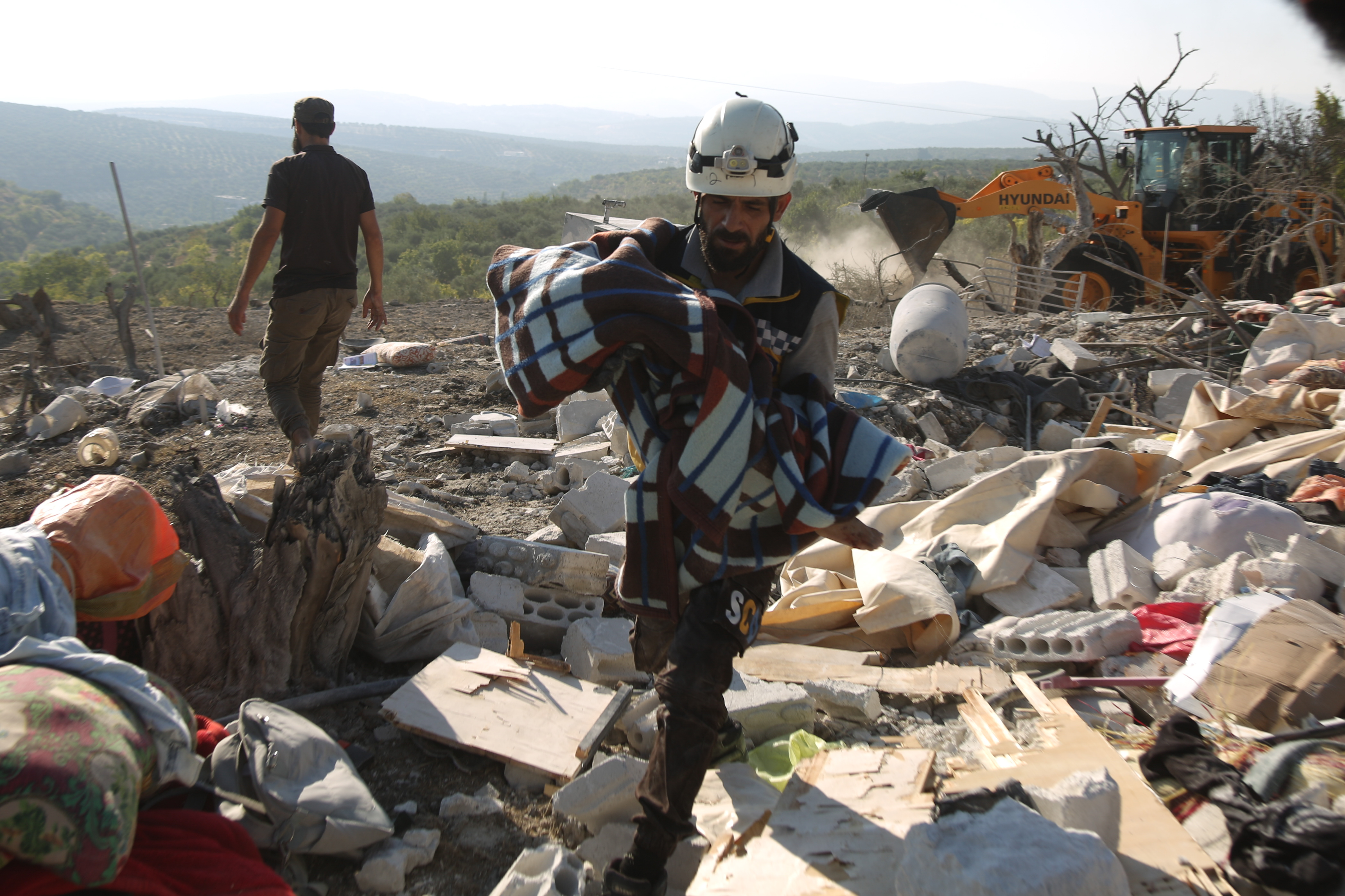 White Helmets member carries a child's body wrapped in a blanket in the middle of rubble