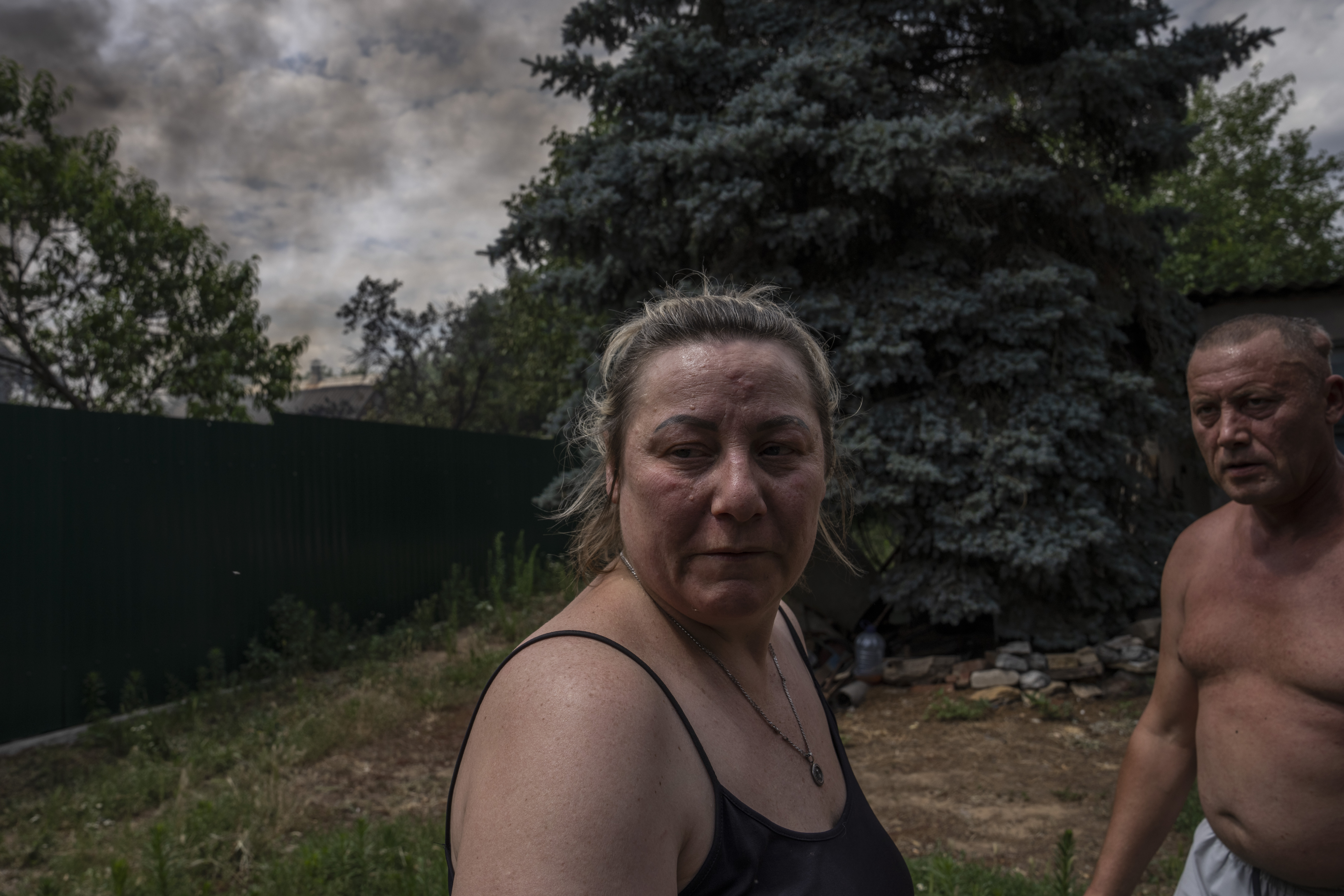 A man and woman look at damages as smoke rises from a house caught on fire, after cluster rockets hit a residential area in Konstantinovka, eastern Ukraine, Saturday, July 9, 2022.