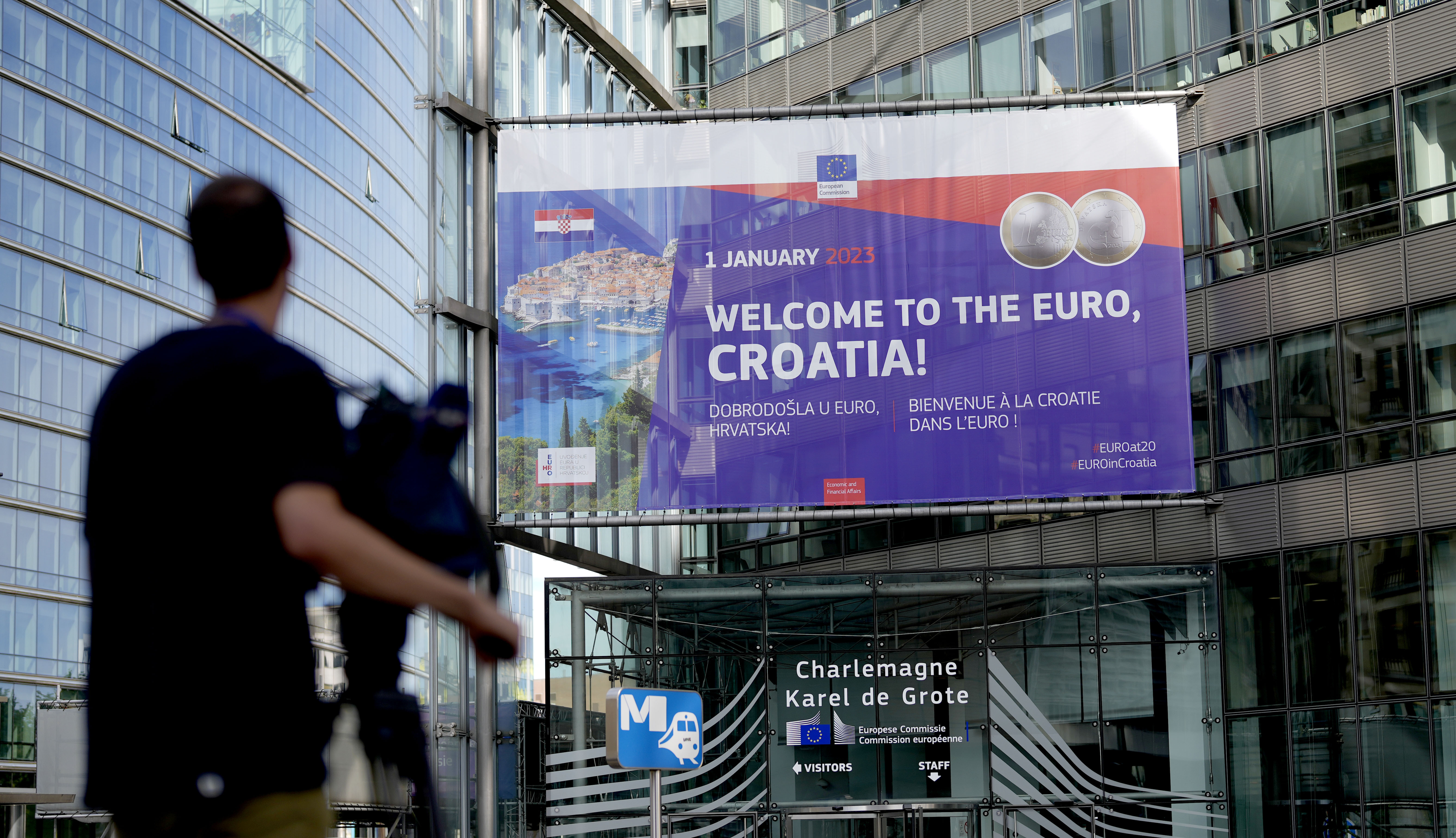 A video journalist films a banner welcoming Croatia to the euro in front of EU headquarters in Brussels