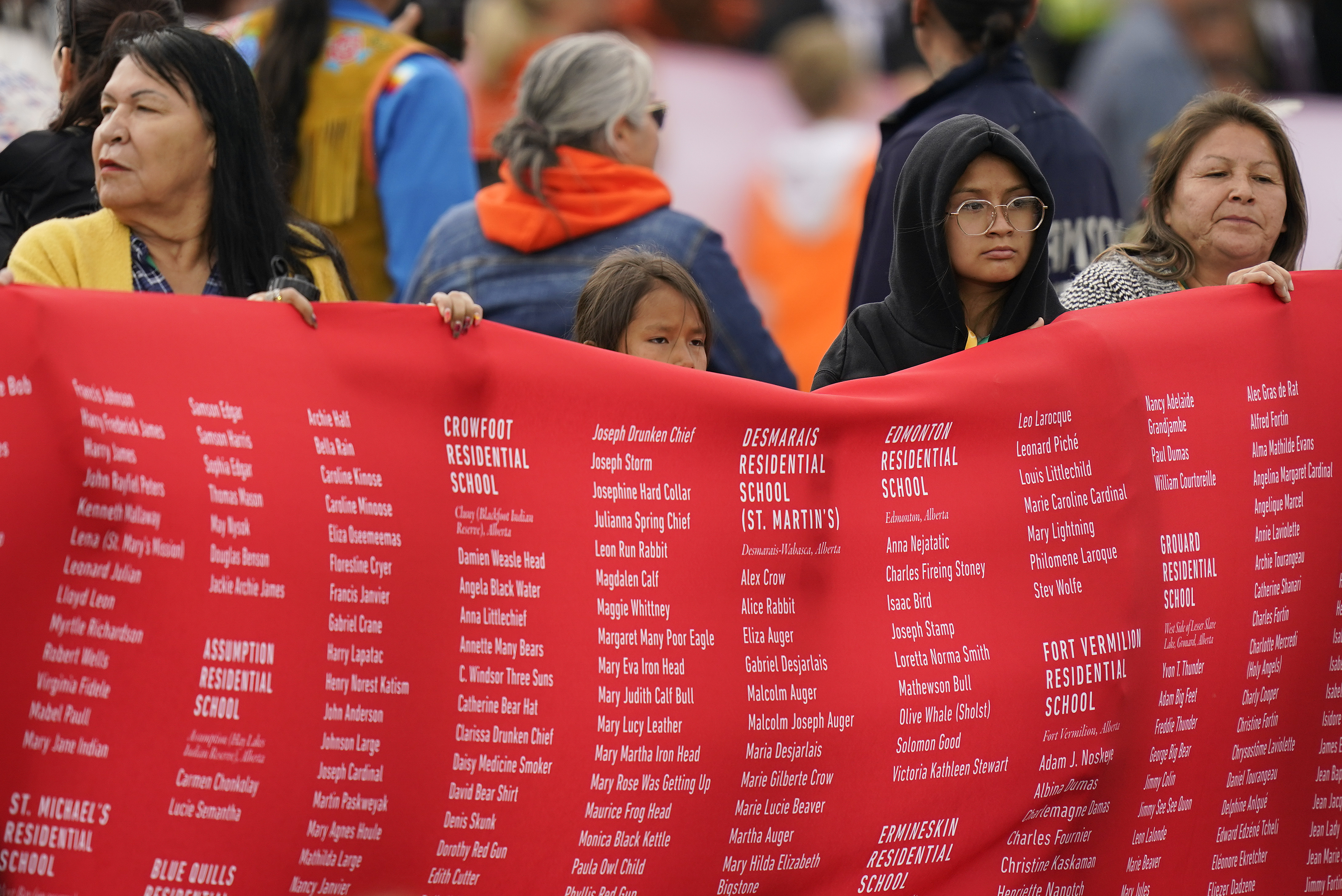 A photo of indigenous people holding up a large red banner that has a long list of names.