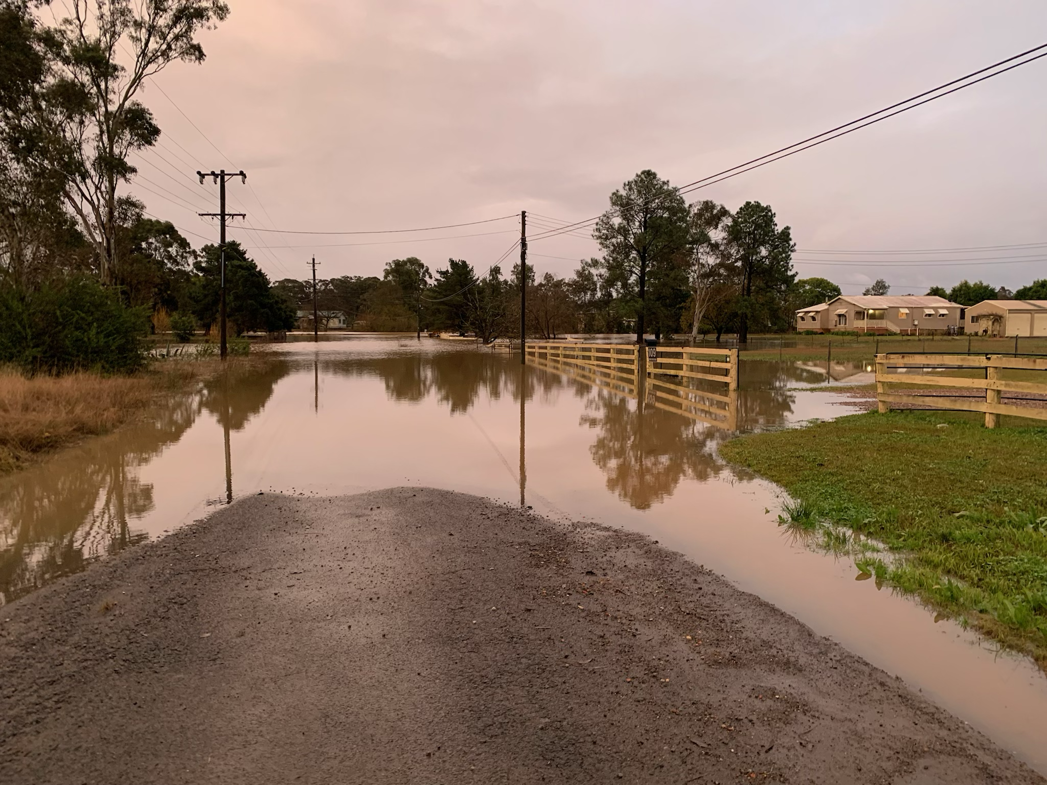 Nena's road disappears beneath flood waters with a few trees in the distance and a patch of grass on the right.