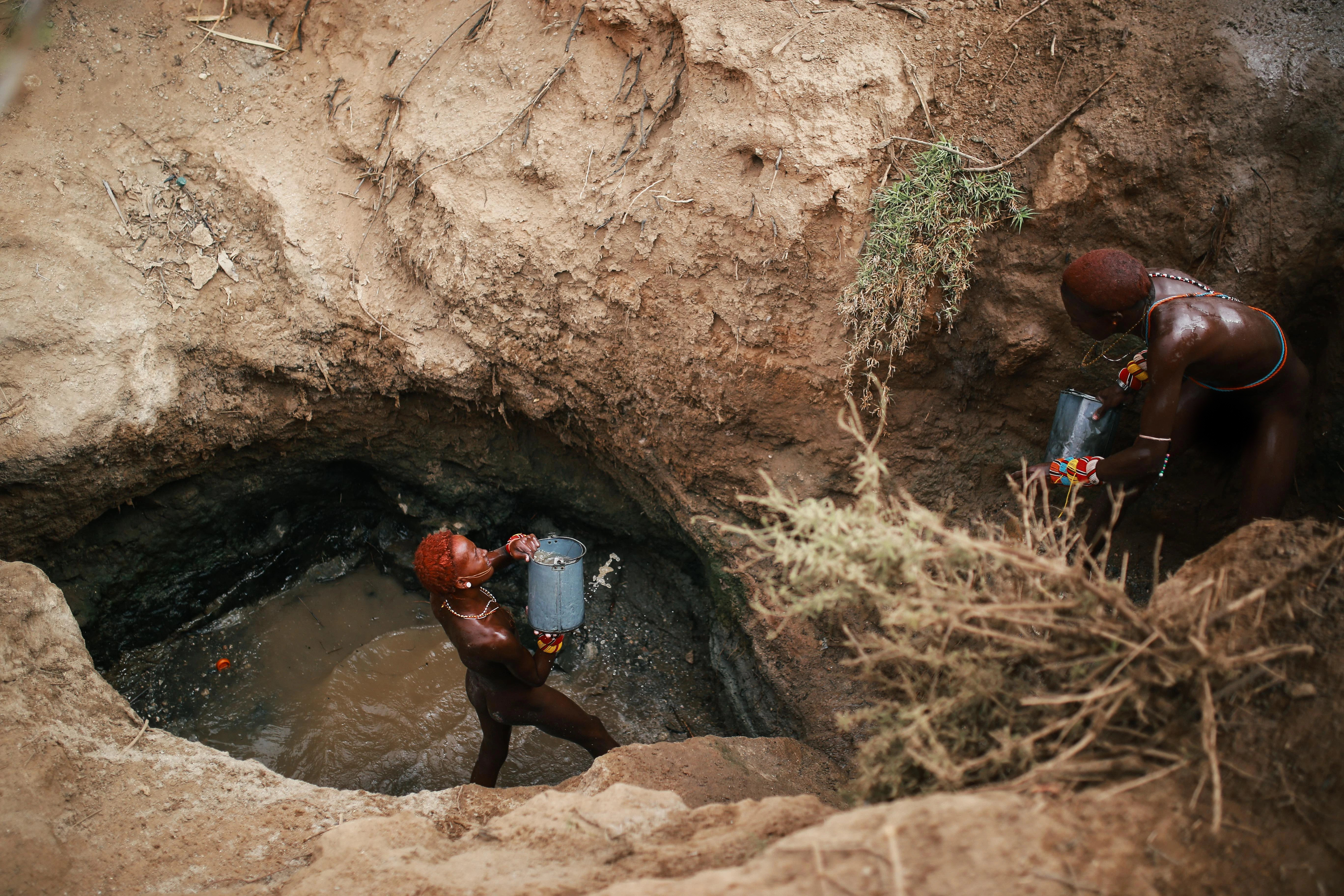 Two herders scoop up water for their animals