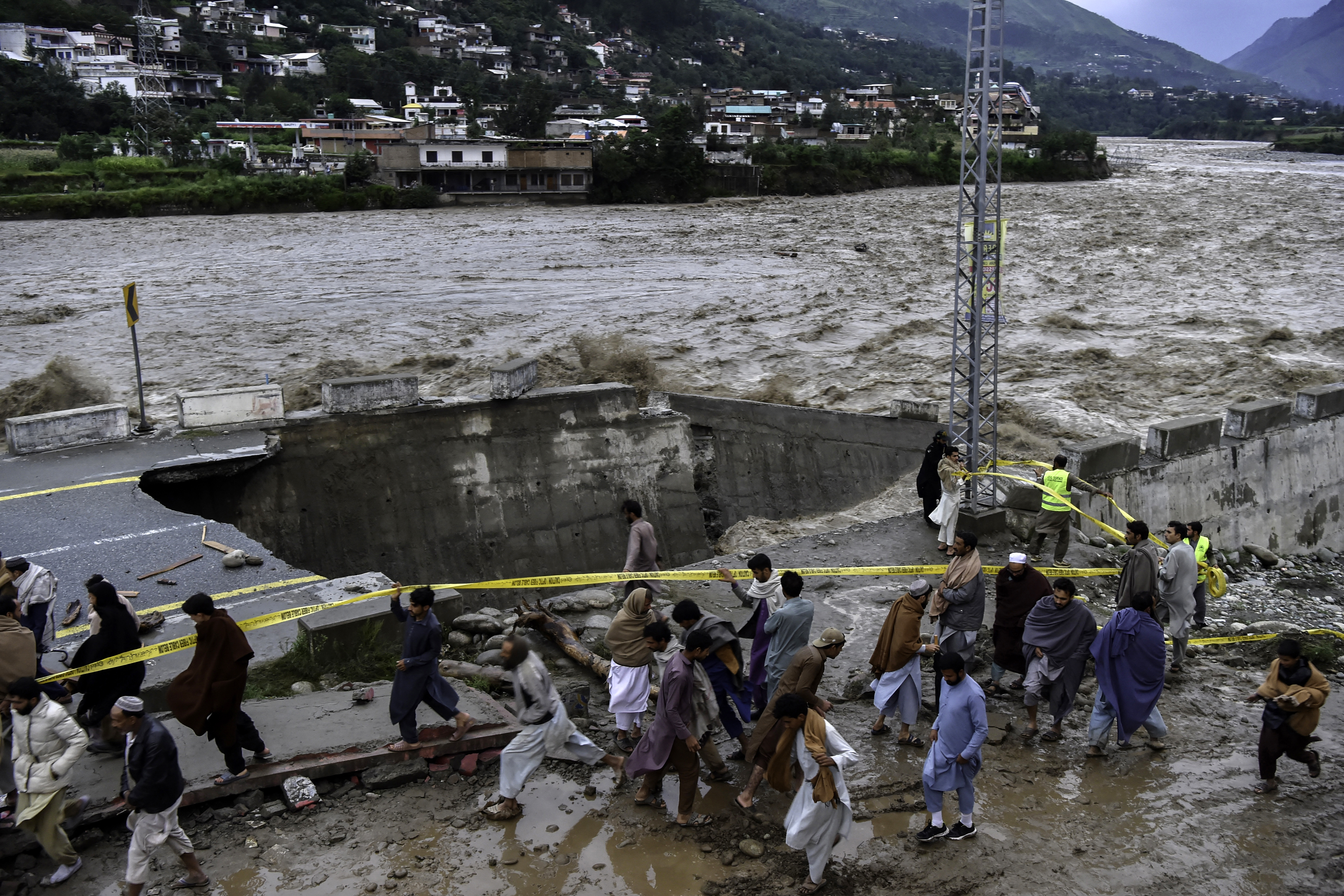 People gather in front of a road damaged by flood