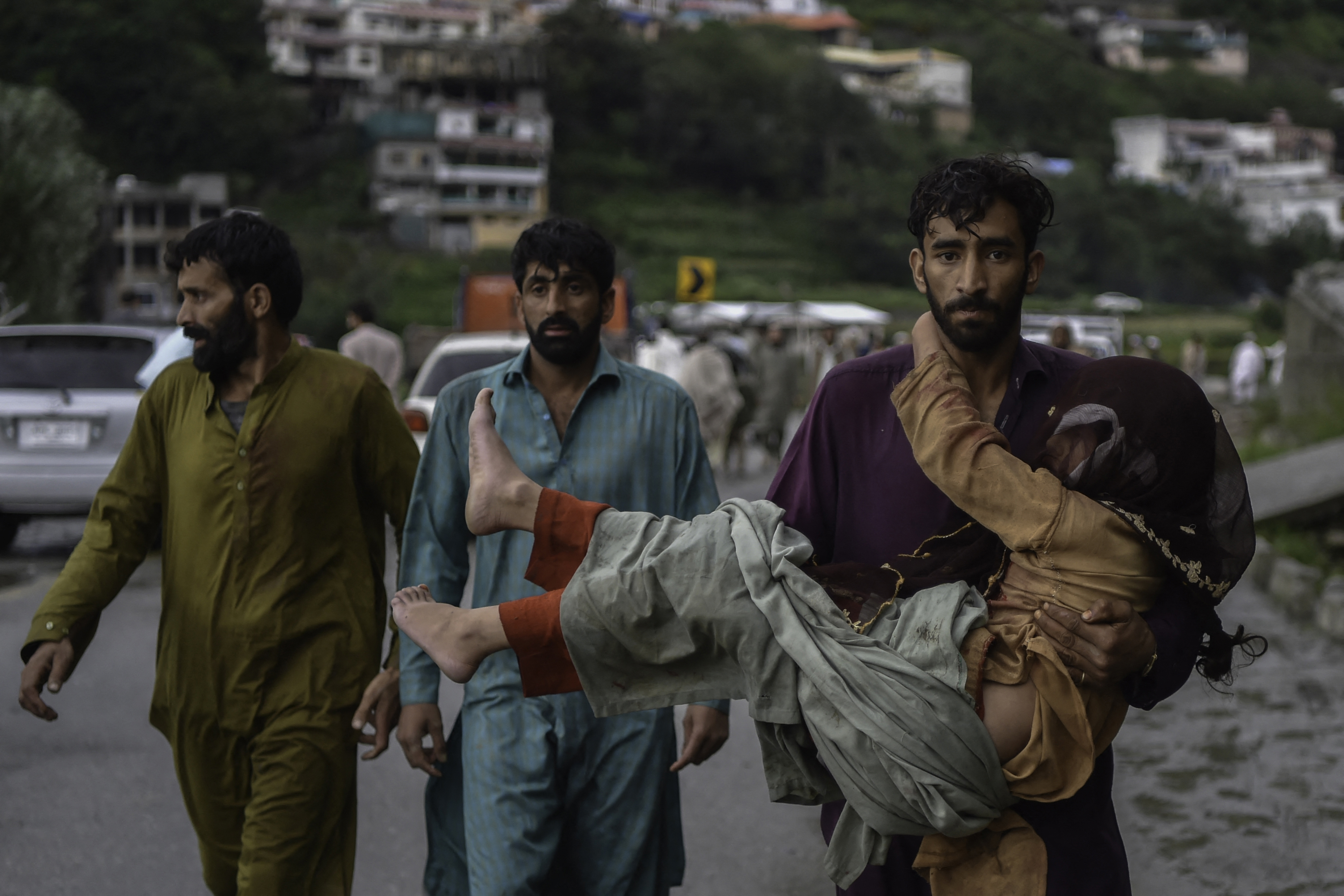 A man (R) carries his sick daughter along a road damaged by flood waters
