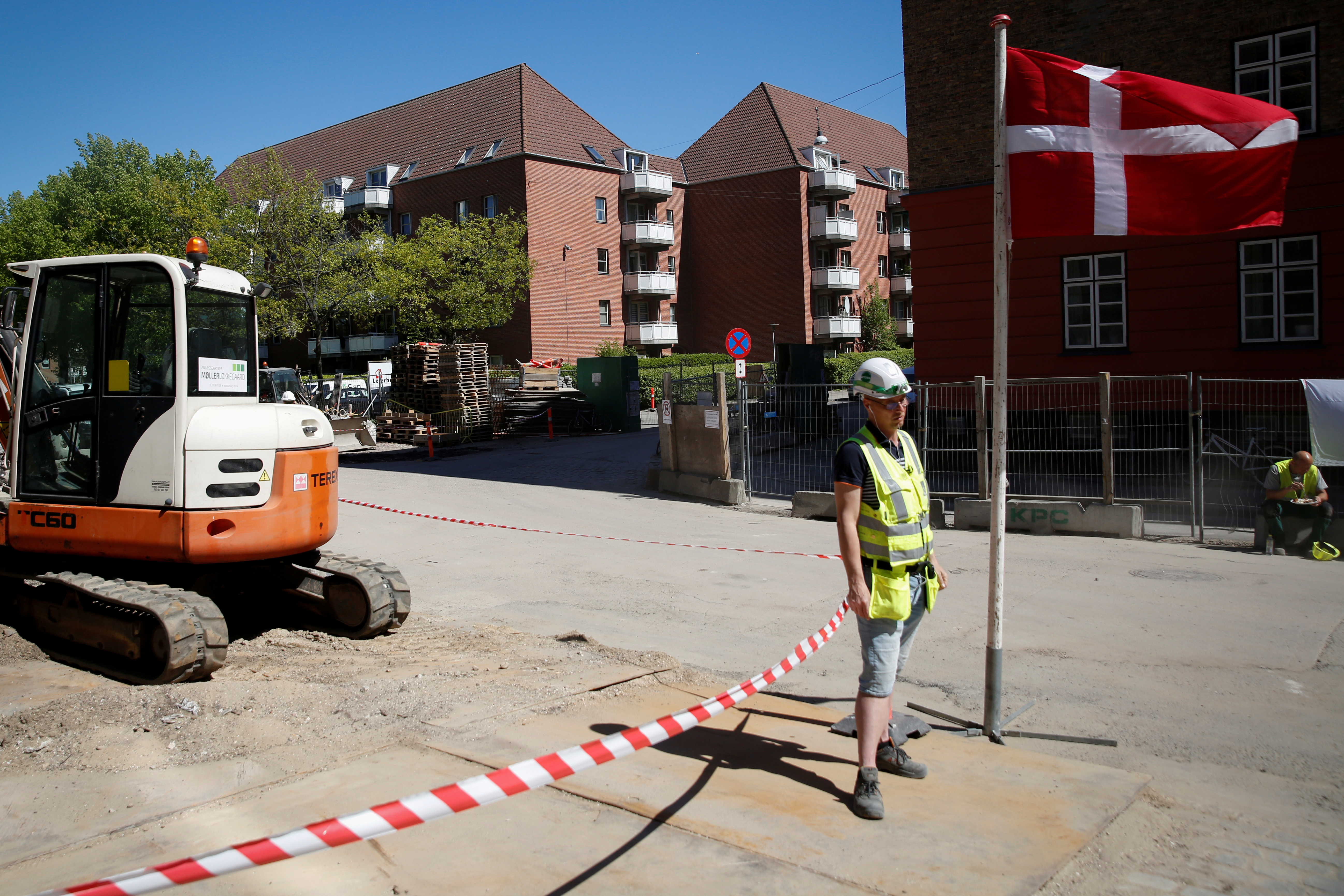 A worker stands beside a Danish flag on a construction site of new housing being built next to Mjolnerparken, a housing estate that features on the Danish government's "Ghetto List", in Copenhagen, Denmark