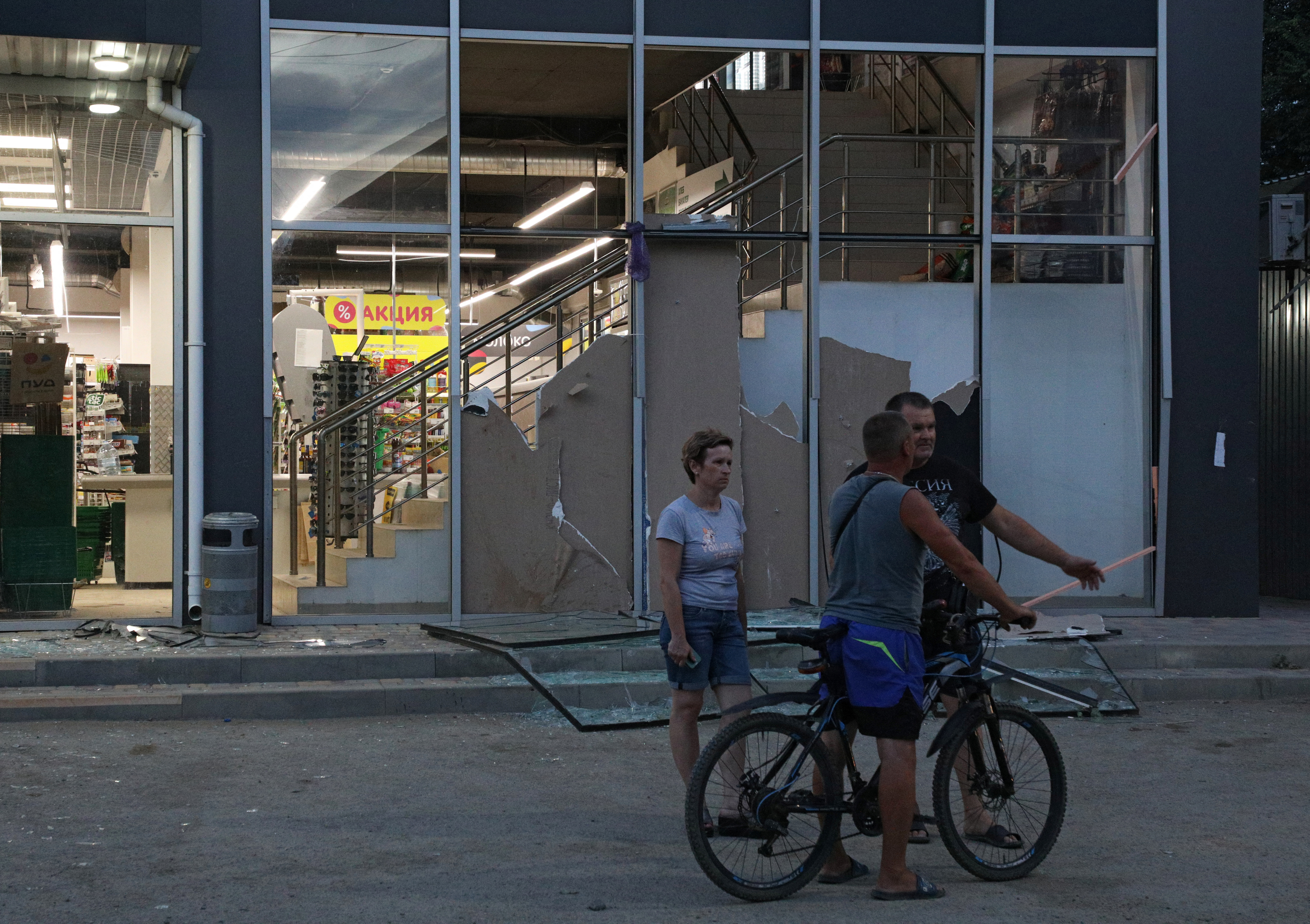 People stand next to a building with windows broken as a result of explosions at a Russian military airbase, in Novofedorivka, Crimea August 9, 2022. REUTERS/Stringer