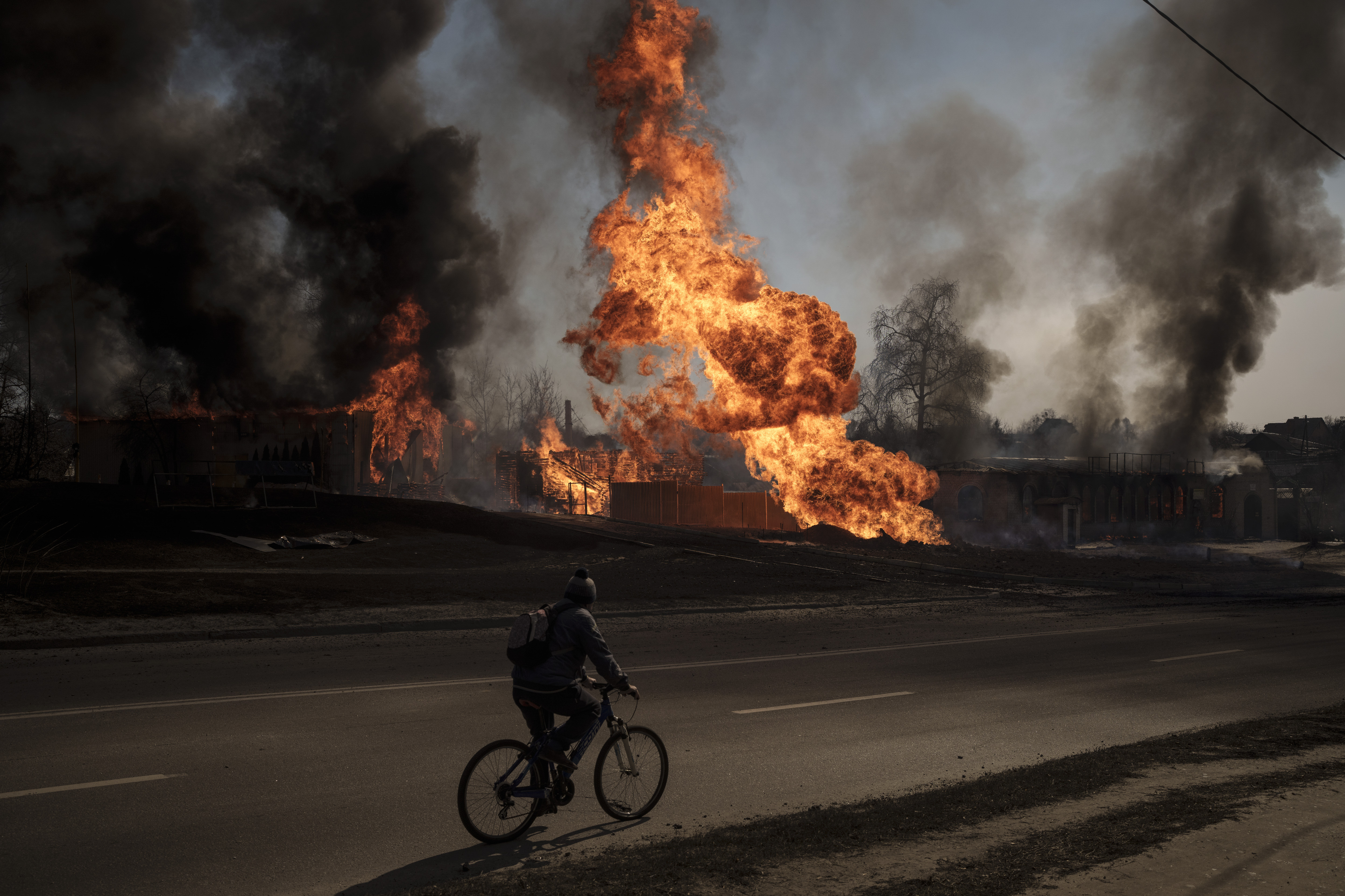 A man rides his bike past flames and smoke rising from a fire following a Russian attack in Kharkiv, Ukraine