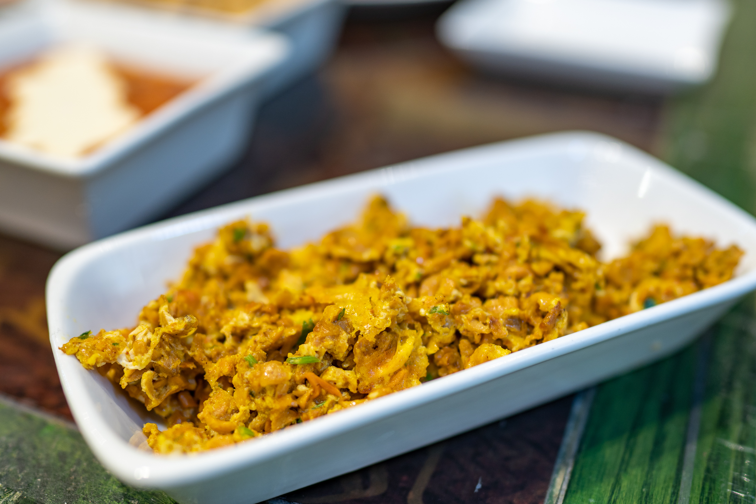 A rectangular bowl of scrambled eggs with mushrooms is shown, the eggs have a slighlty yellowish tint and finely chopped veggies can be seen